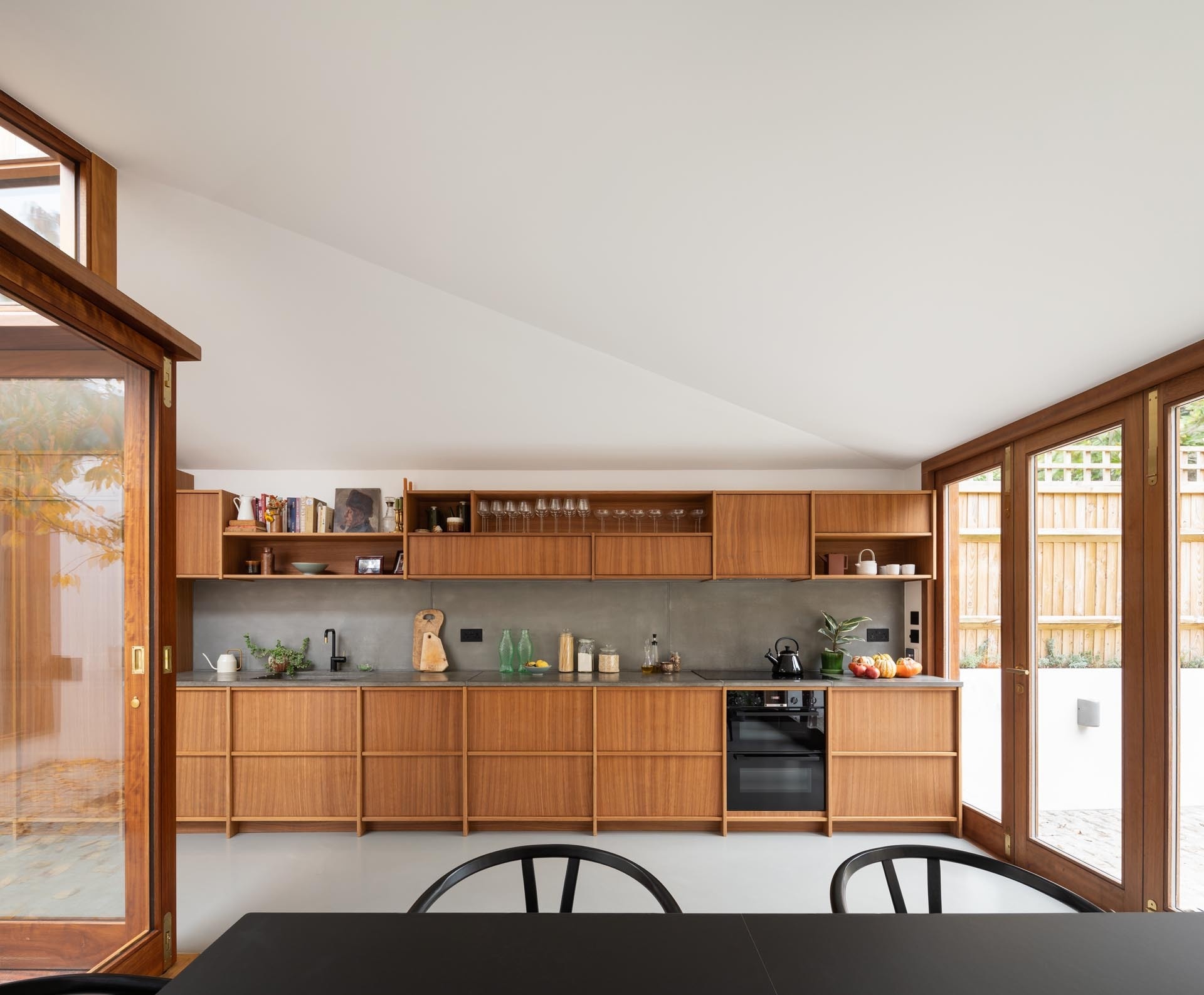 A minimalist wood kitchen with handle-free cabinets and a dark gray backsplash keeps the look clean and modern.