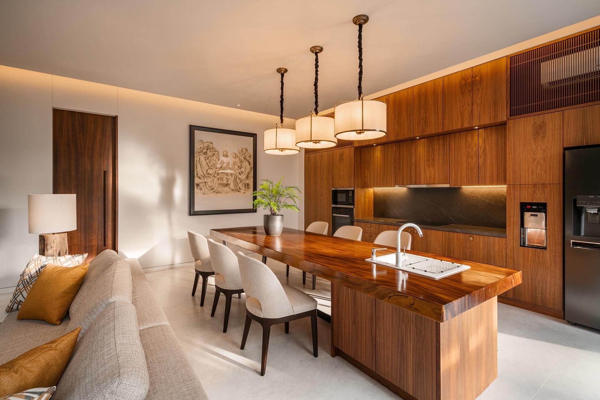 This space flows directly into the kitchen and dining area, forming a large open-plan layout. The kitchen itself is defined by warm wood finishes, with the dining area seamlessly integrated into the island, creating a social and practical hub.