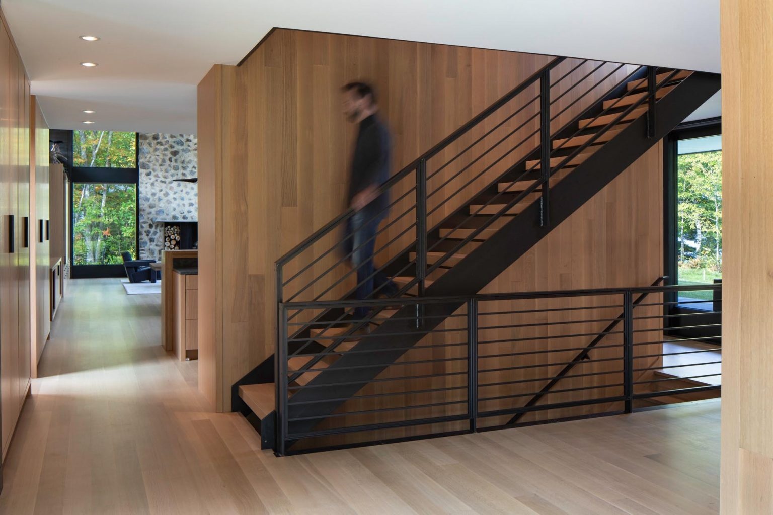 Una escalera con barandillas de metal y peldaños de roble blanco conecta los múltiples niveles de una moderna casa en el lago.