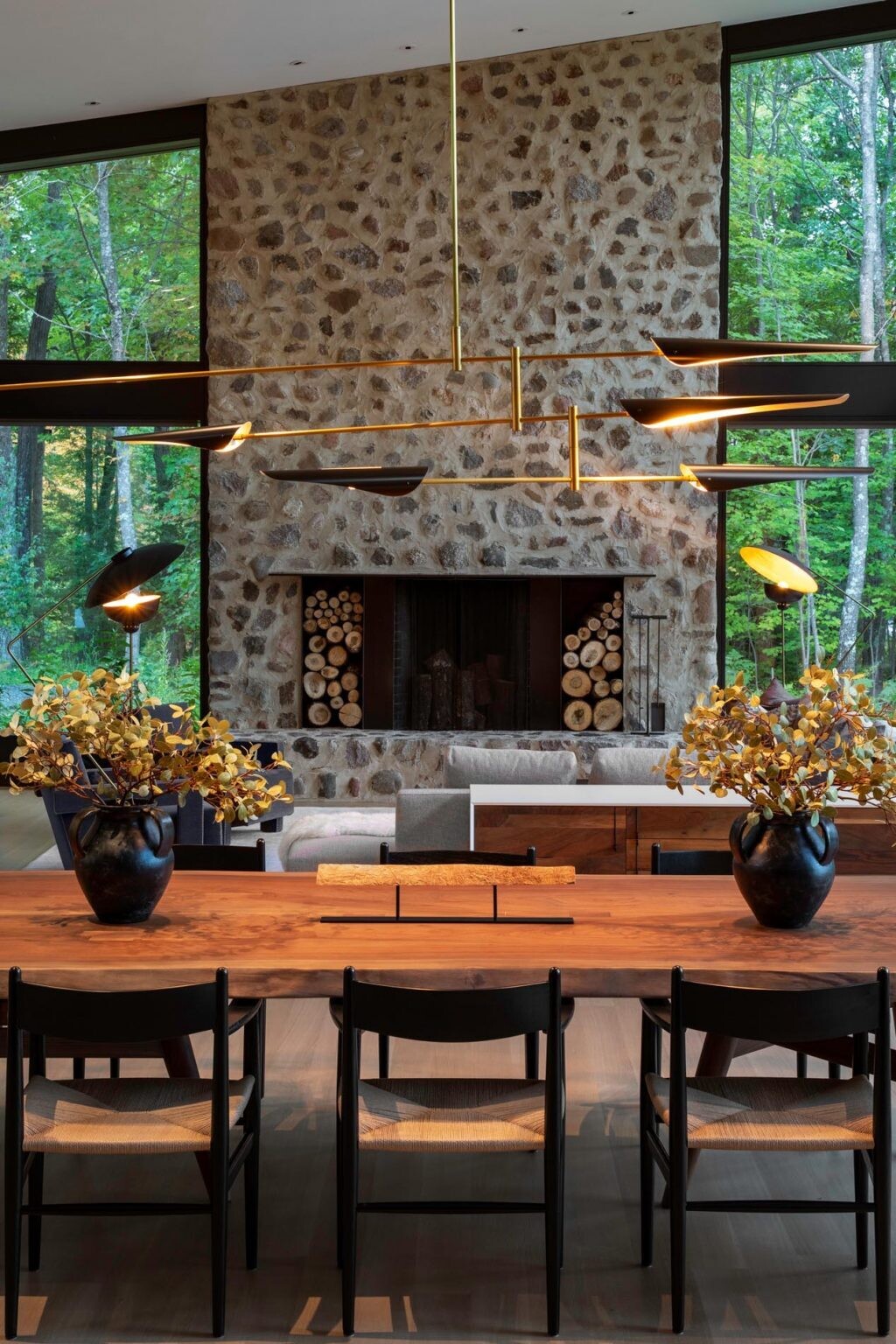 Una mesa de comedor de madera personalizada se combina con una lámpara de araña escultural y ofrece vistas a la espectacular chimenea de piedra.
