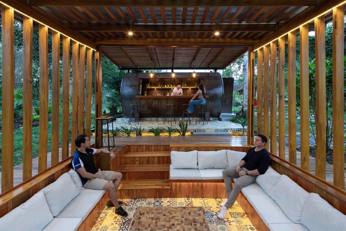 A sunken conversation pit surrounded by timber decking creates a cosy outdoor lounge that glows with soft lighting at night.