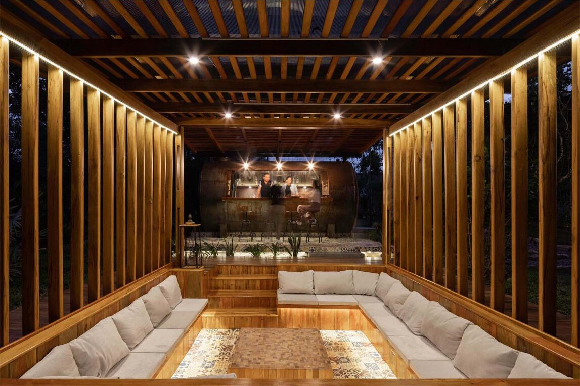 A sunken conversation pit surrounded by timber decking creates a cosy outdoor lounge that glows with soft lighting at night.