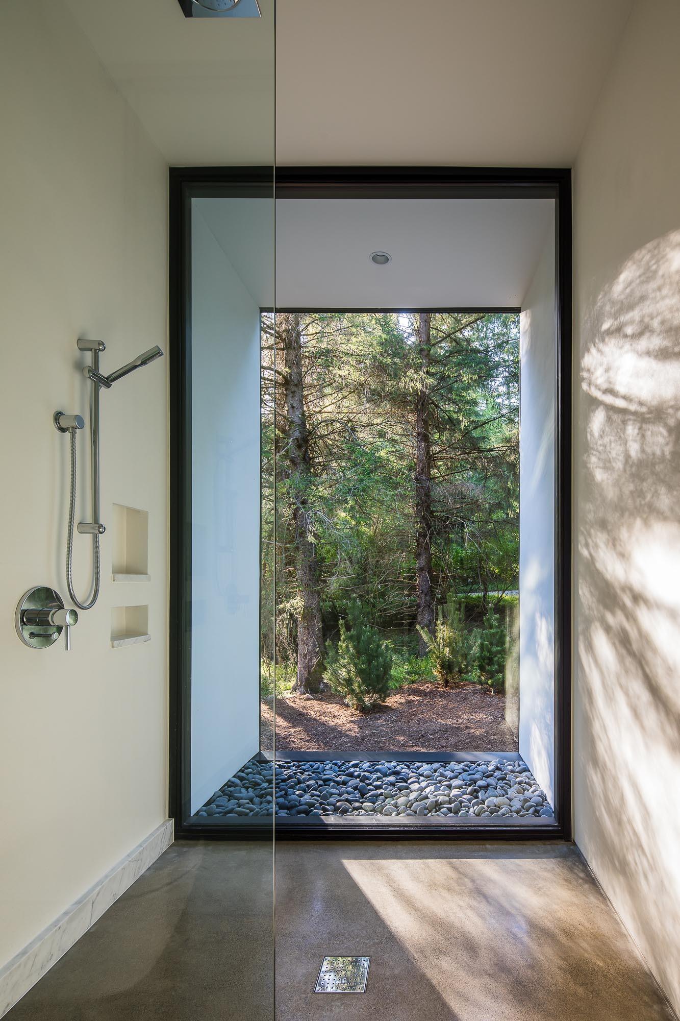 A modern bathroom has a shower positioned to look directly out toward the trees, adding a natural view into the experience.
