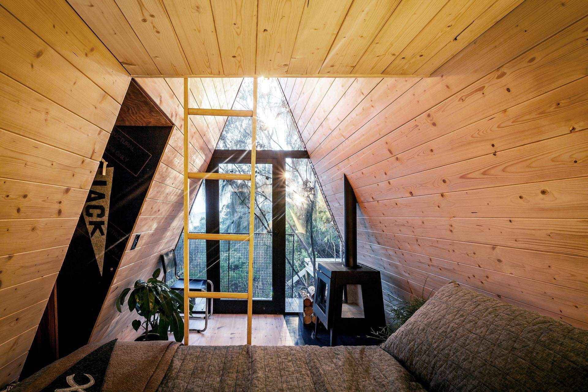 Inside this A-frame cabin, Baltic Pine walls, a floating daybed, fireplace, and loft create a compact yet flexible living space.