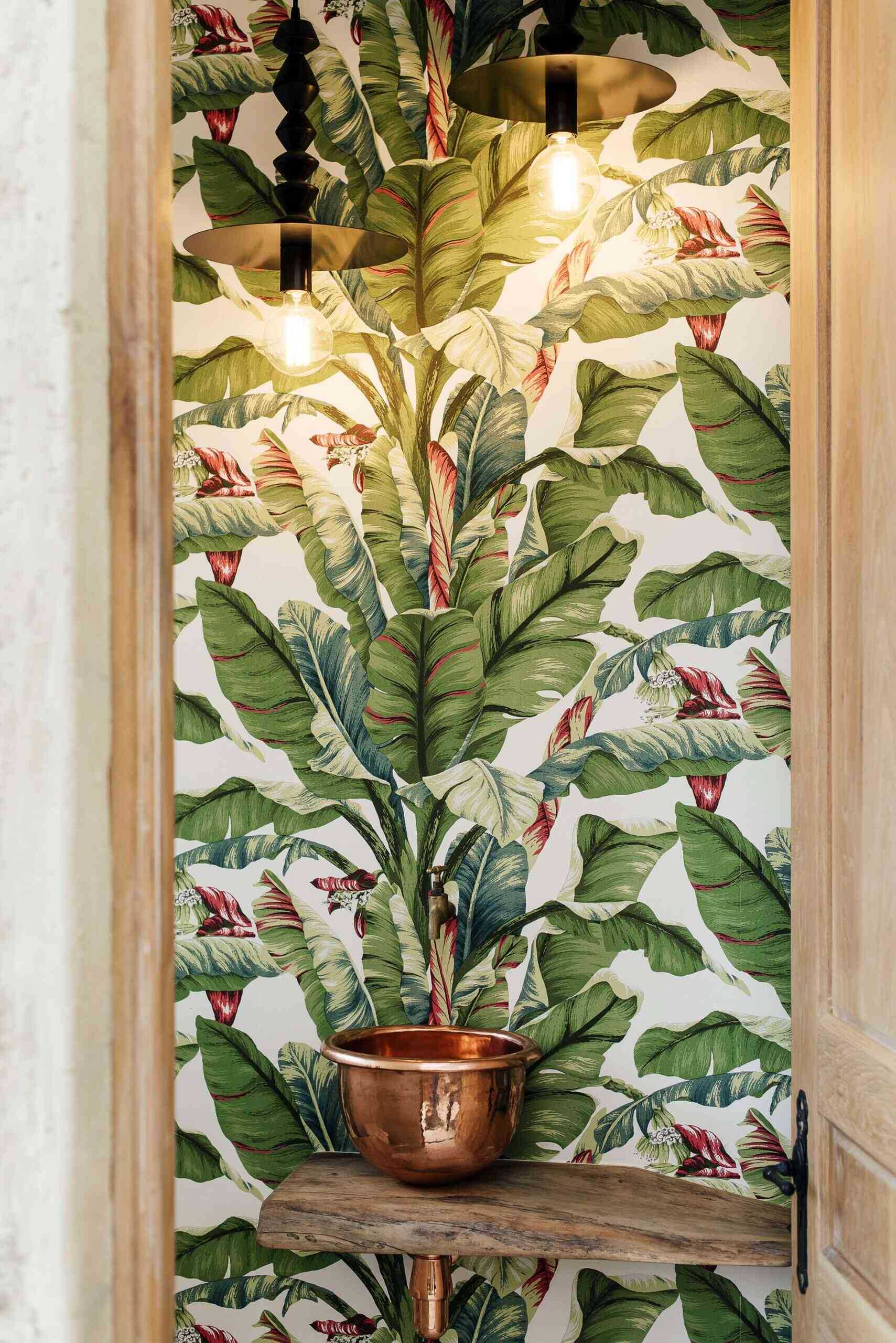 A compact powder room surprises with tropical wallpaper, adding contrast to the home’s clean material palette.