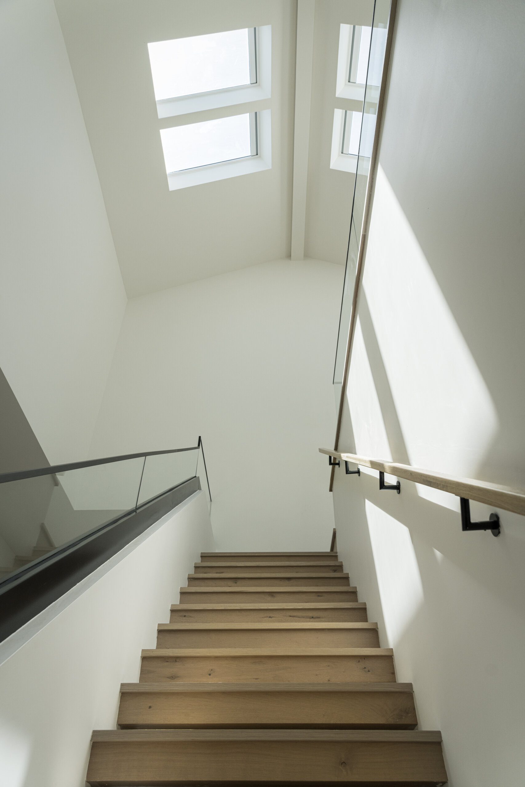 A double-height stair volume becomes a key feature of the home. Skylights above act as vertical light wells, pulling daylight down through the levels and helping the interior feel open despite the compact footprint.