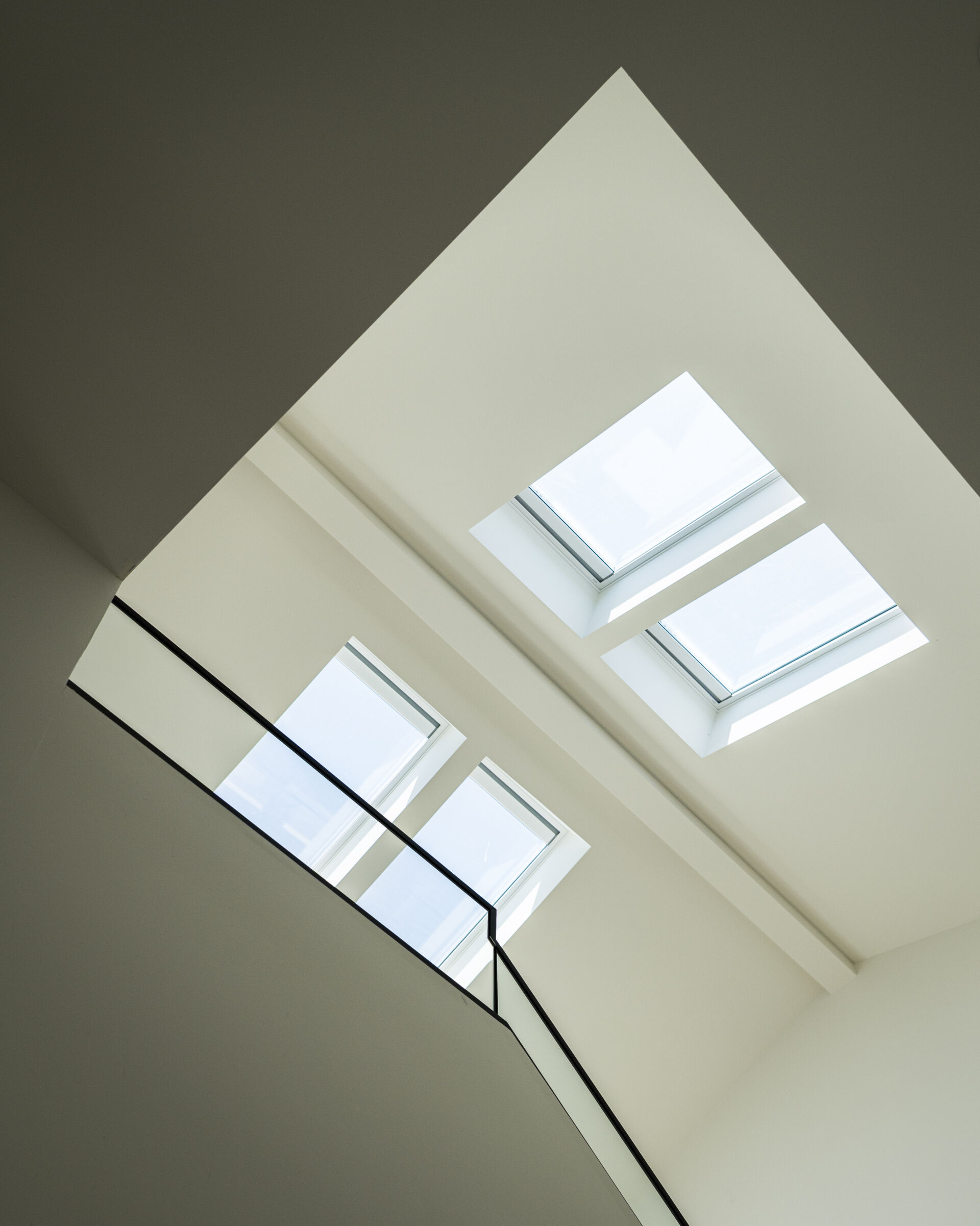A double-height stair volume becomes a key feature of the home. Skylights above act as vertical light wells, pulling daylight down through the levels and helping the interior feel open despite the compact footprint.