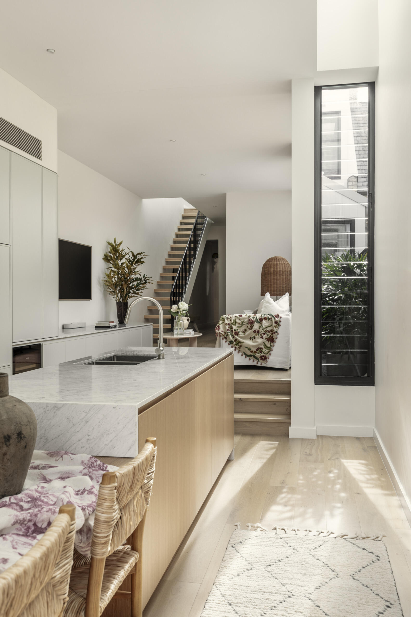 Built-in storage is integrated throughout, keeping the space uncluttered and functional. These elements blend into the architecture, maintaining the clean aesthetic.
A subtle change in level, marked by steps, leads up into the living room, creating a gentle separation without closing off the space.