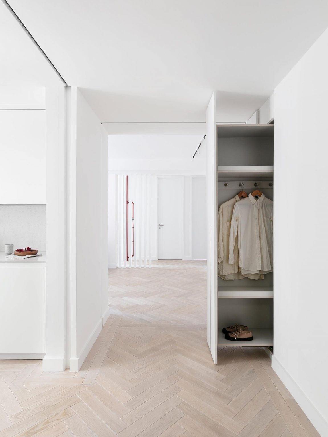 Hidden storage in the hallway with pull-out cabinets and updated oak herringbone flooring.