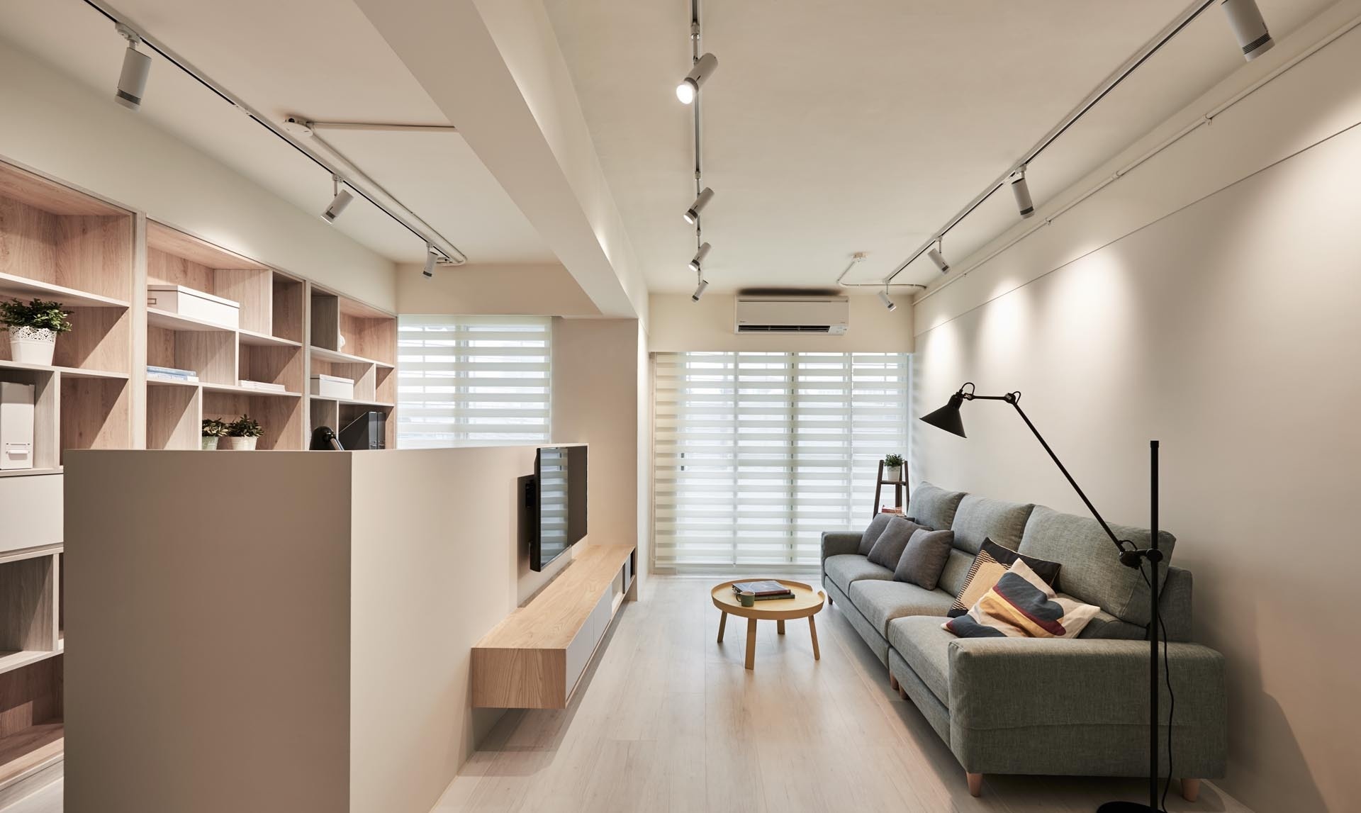A living room in Taiwan that doubles as a home office, featuring a hidden desk, wood-lined bookshelves, and a sleek floating TV wall.