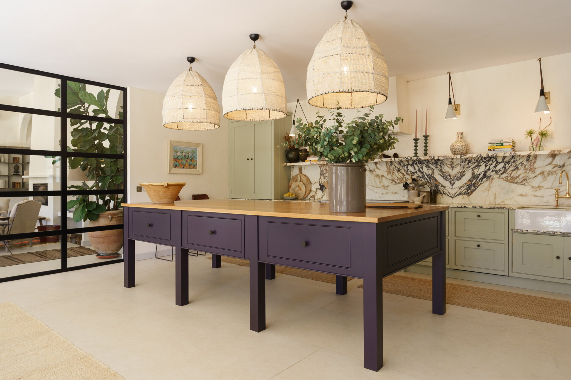 This contemporary kitchen combines sage cabinetry, dramatic marble, woven pendant lights, and a bold plum island for a warm Mediterranean-inspired look.