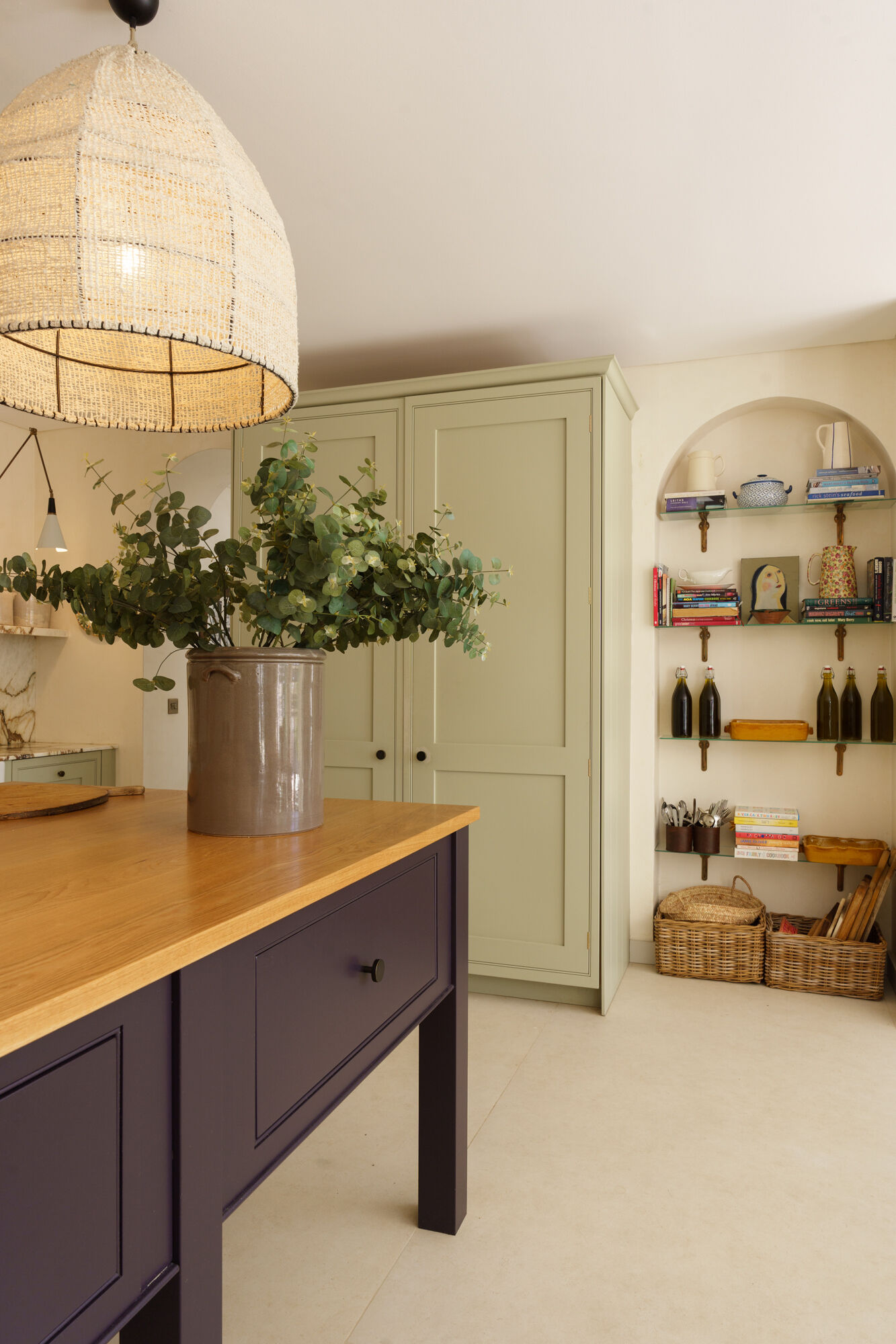 This contemporary kitchen combines sage cabinetry, dramatic marble, woven pendant lights, and a bold plum island for a warm Mediterranean-inspired look.