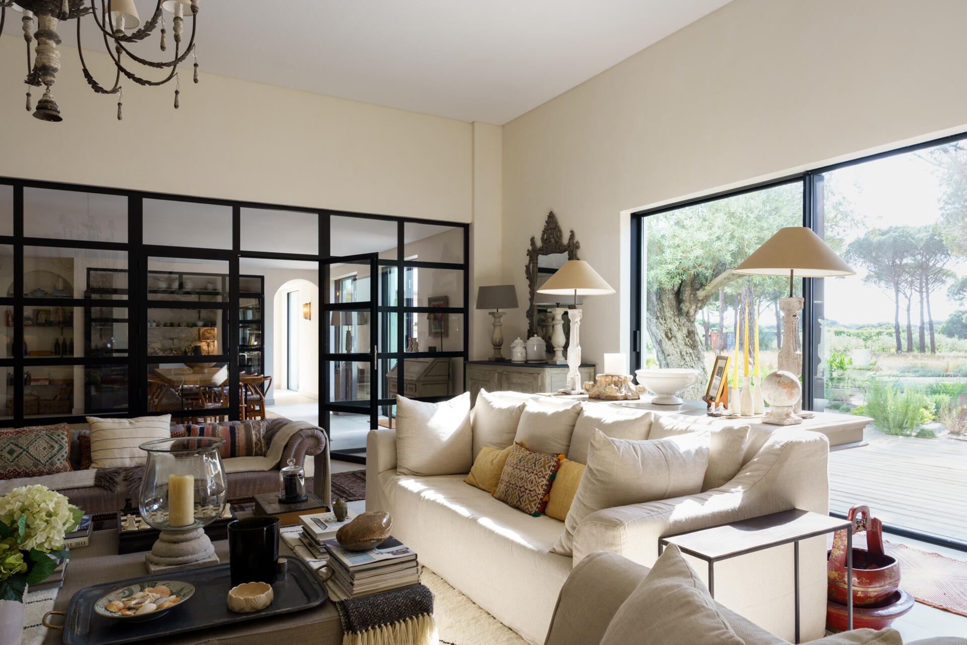 Inside the central wing of the villa, the living room opens completely toward the courtyard through expansive retractable glazing. The room feels constantly linked to the outdoors. Even when closed, the glass walls maintain uninterrupted views of trees, sand, and sky from nearly every angle.