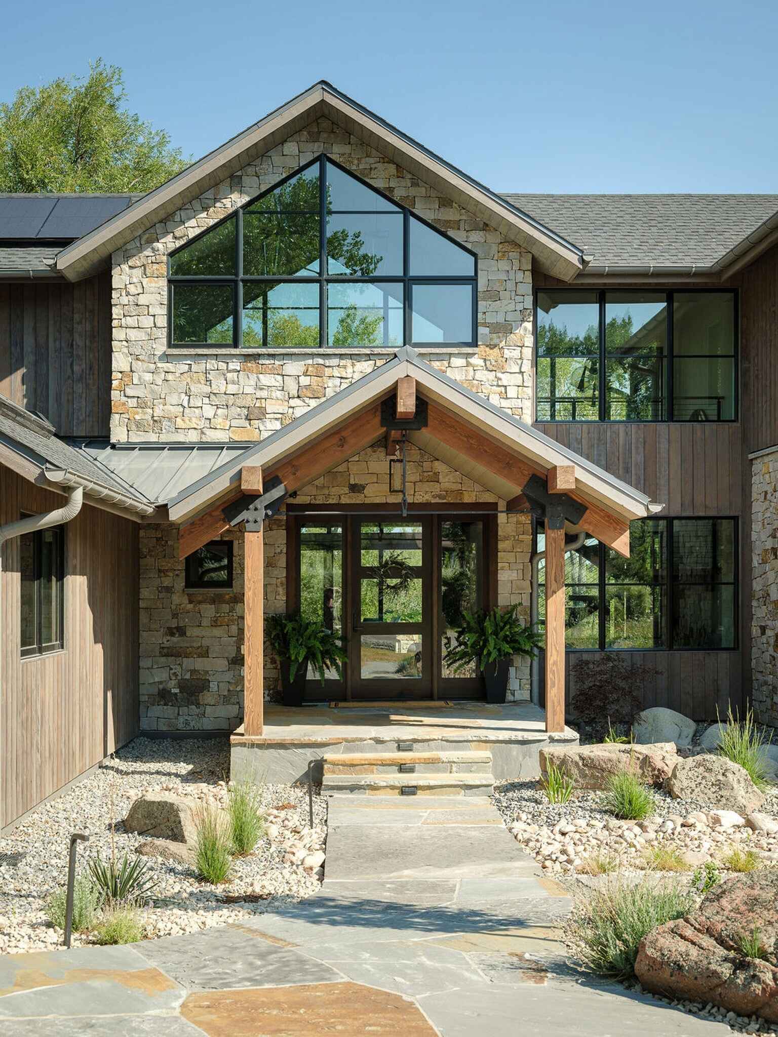 Stone walls, exposed timber beams, and dramatic gabled windows shape the welcoming entrance of this modern Boulder mountain home.
