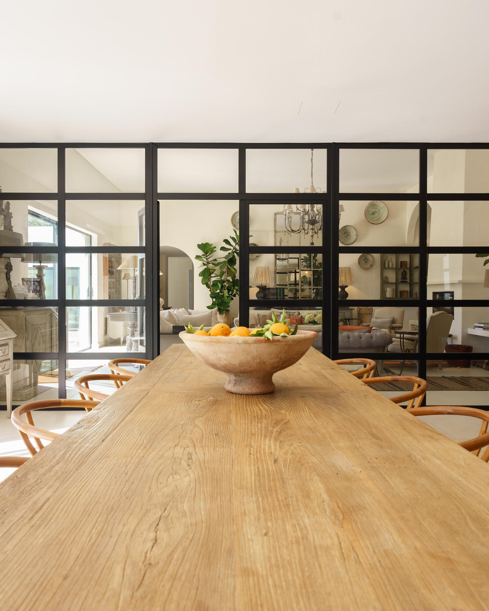 The dining space is separated from the living room by a black-framed glass wall, allowing for natural light to pass through and provide views of the living room.