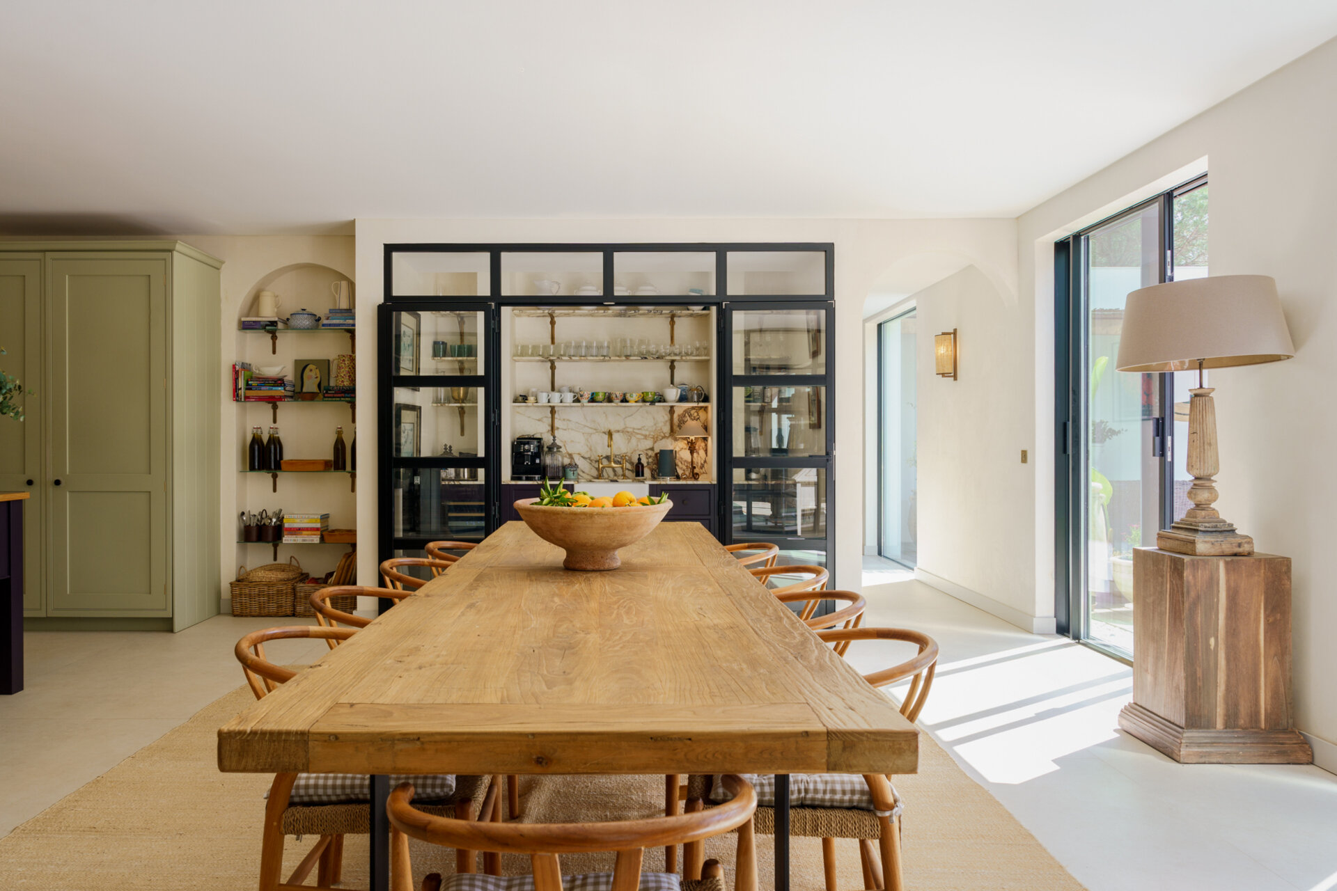 The dining space is separated from the living room by a black-framed glass wall, allowing for natural light to pass through and provide views of the living room.