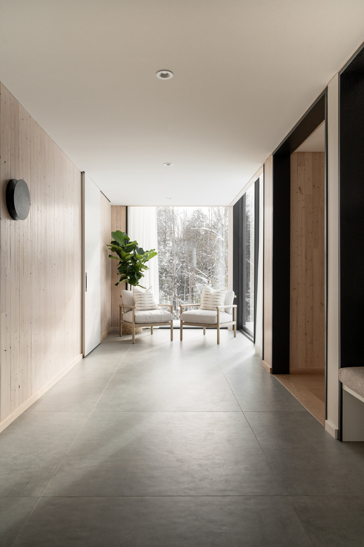 A glass-lined hallway that connects separate volumes, while also including a dedicated area for shoes, coats, storage, and benches.