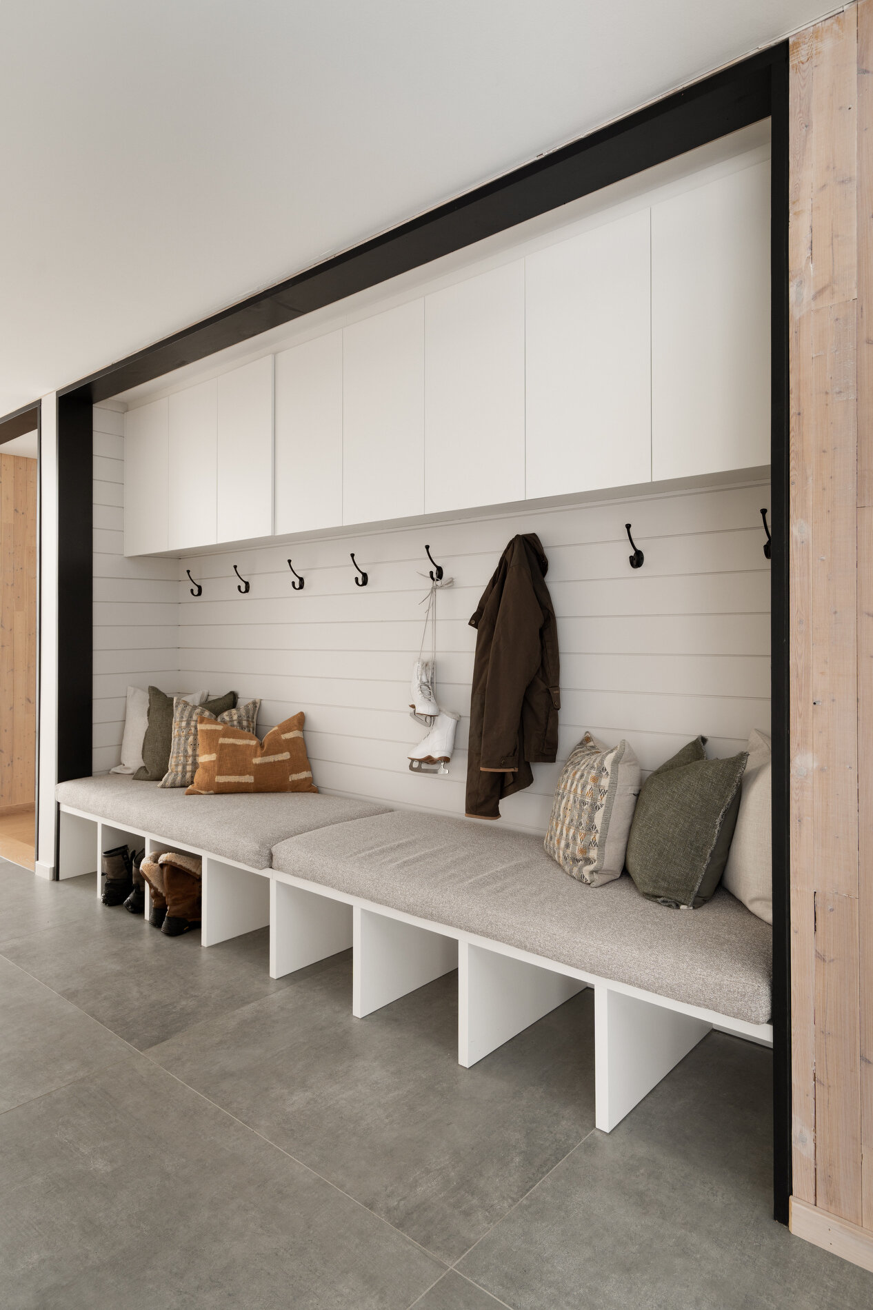 A glass-lined hallway that connects separate volumes, while also including a dedicated area for shoes, coats, storage, and benches.