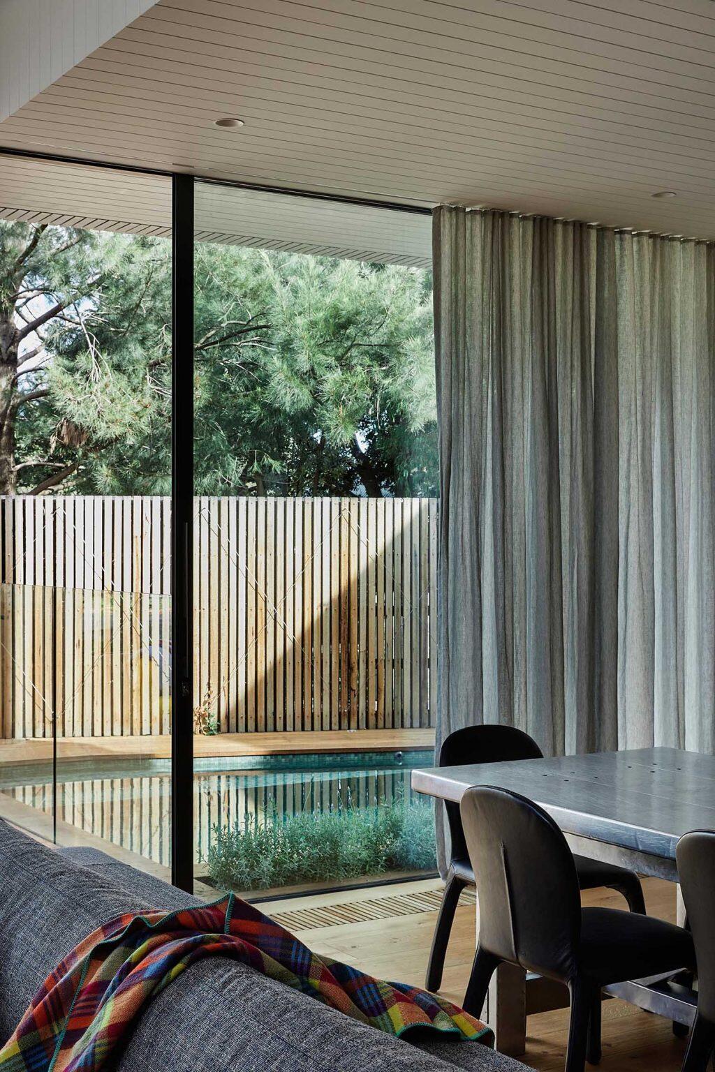 This open-plan Melbourne living space connects directly to an outdoor deck and green plunge pool through massive sliding glass doors and floor-to-ceiling windows.