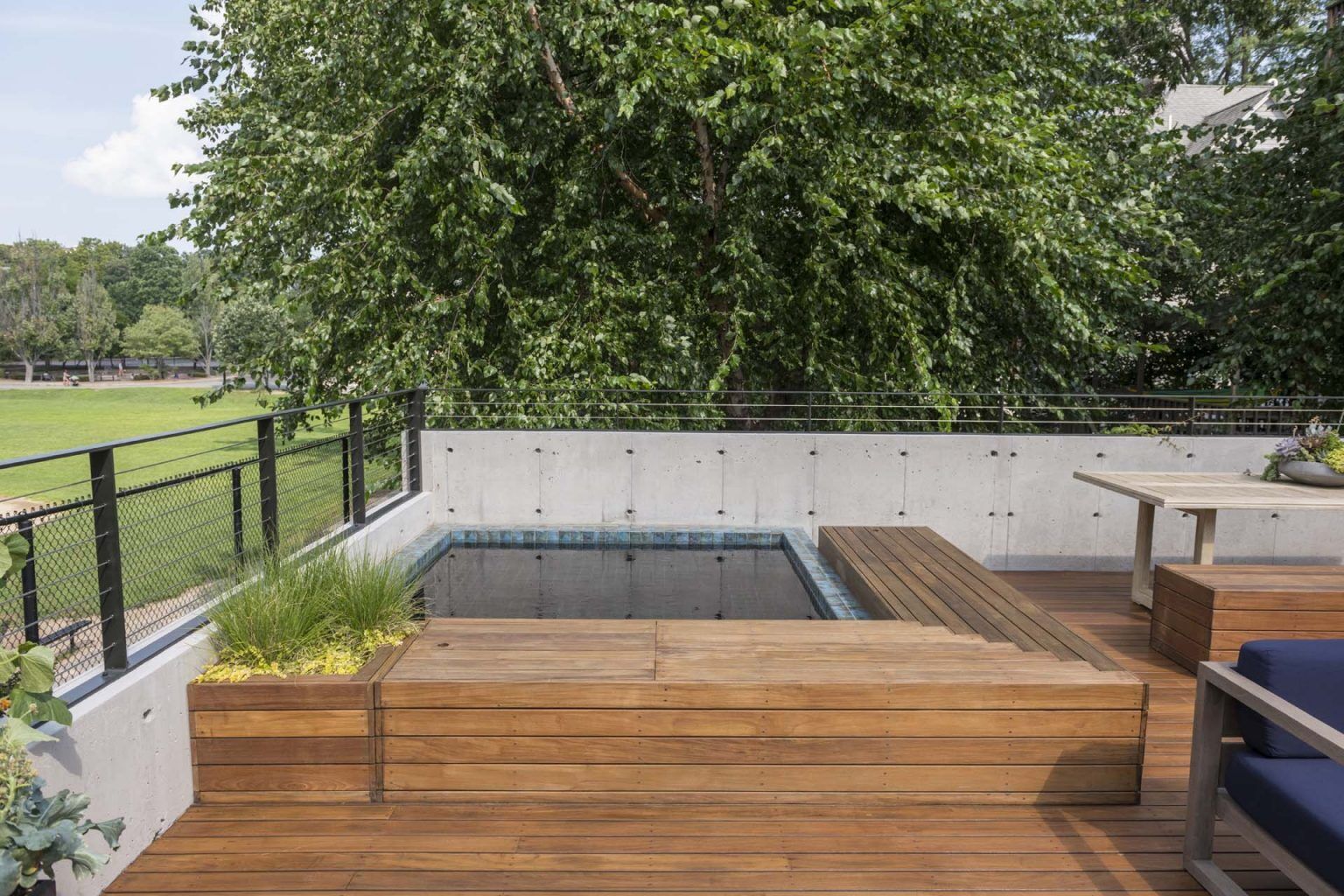 This Ipe rooftop deck features built-in seating, lush planters, and a recessed hot tub overlooking a modern courtyard garden.