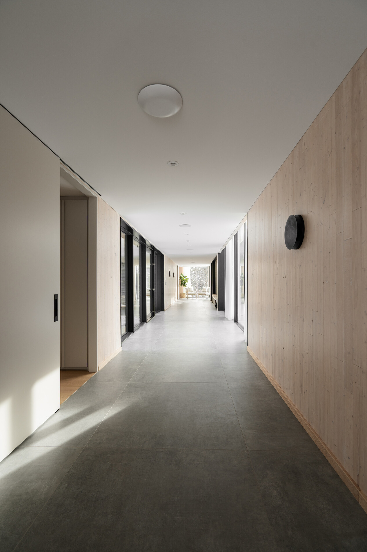 A glass-lined hallway that connects separate volumes, while also including a dedicated area for shoes, coats, storage, and benches.