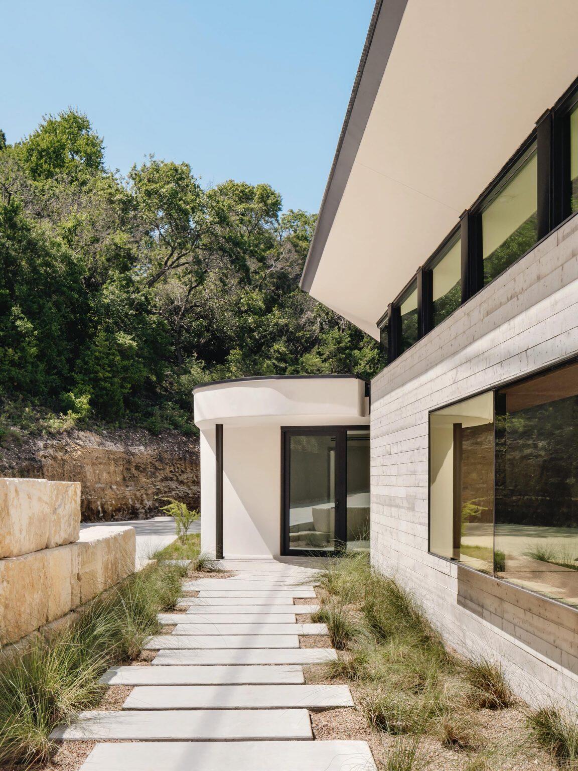 Board-formed concrete walls, grasses, and warm wood details shape the entrance to this modern Austin home.