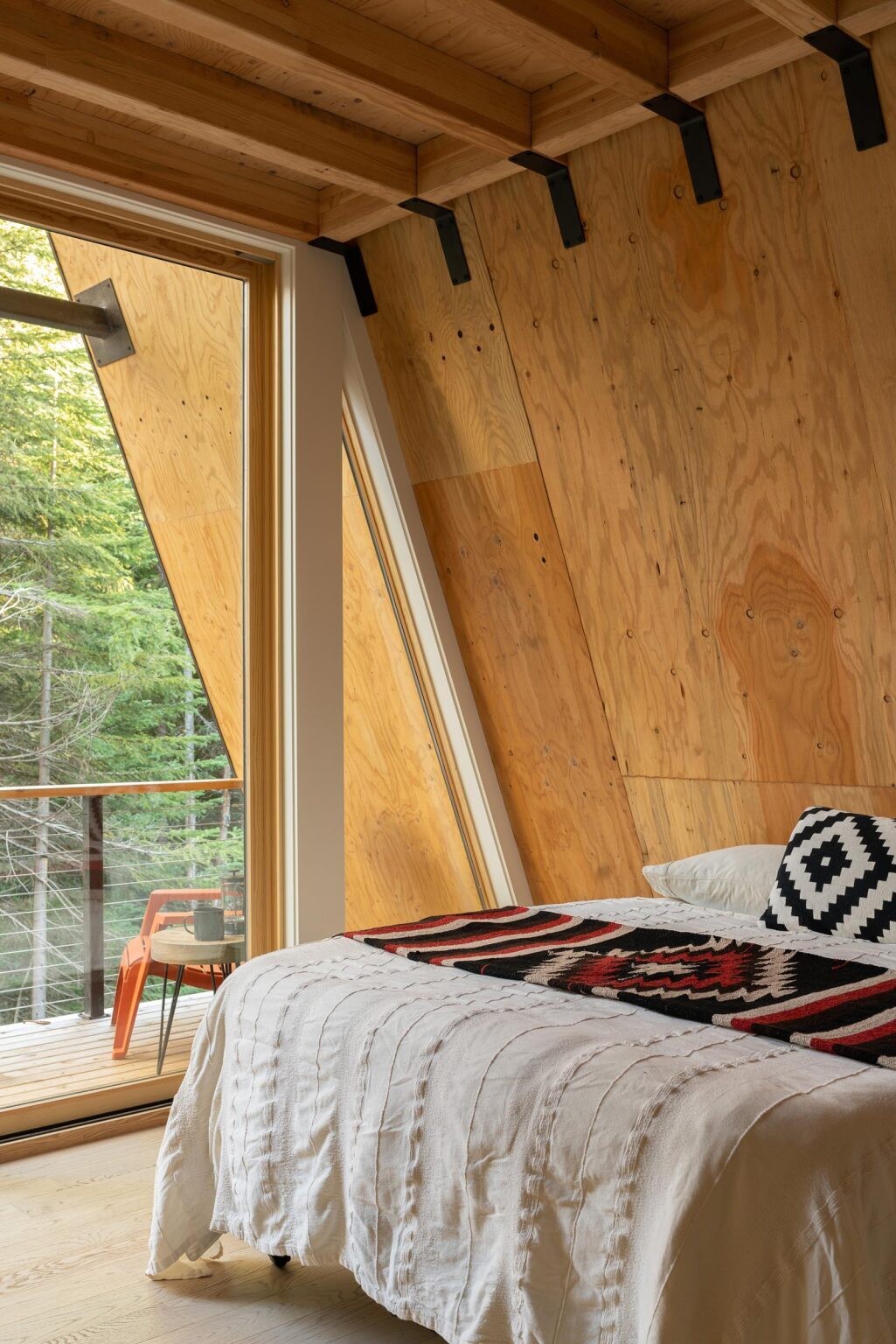 The upstairs bedrooms of this Washington A-frame cabin feature angled ceilings and large roofline windows with peaceful forest views.