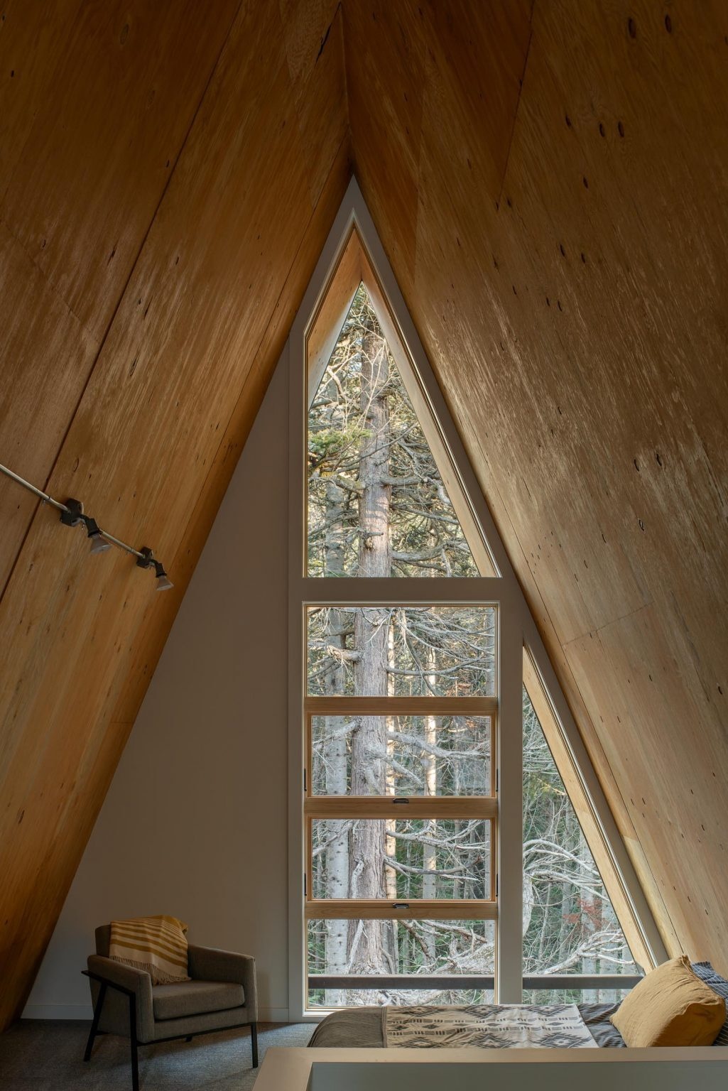 The upstairs bedrooms of this Washington A-frame cabin feature angled ceilings and large roofline windows with peaceful forest views.