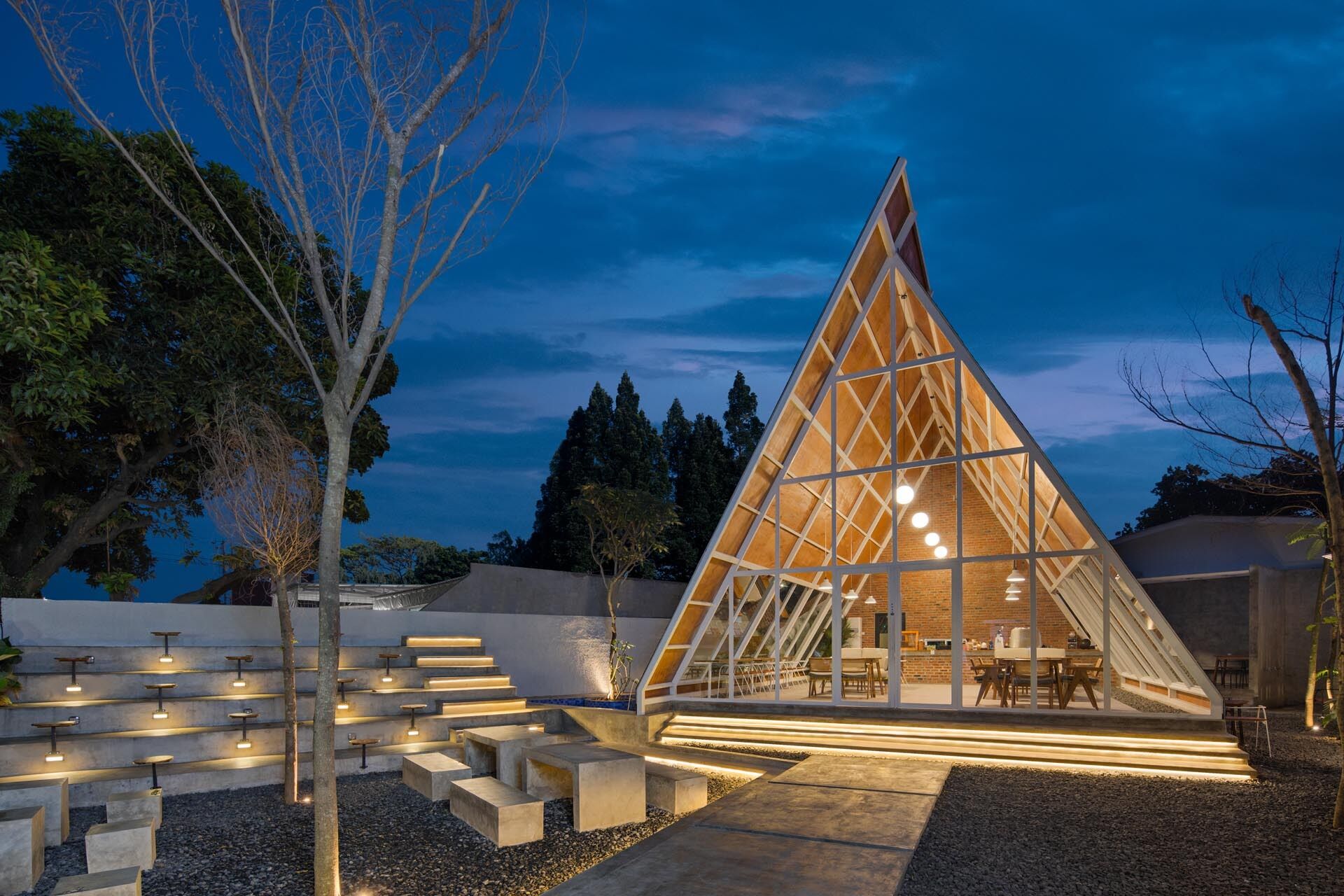 A striking triangular coffee shop in Jakarta, Indonesia, designed by STUDIÉ with exposed concrete, terrazzo floors, brick accents, and dramatic A-frame architecture that transforms a simple geometric idea into a memorable cafe experience.