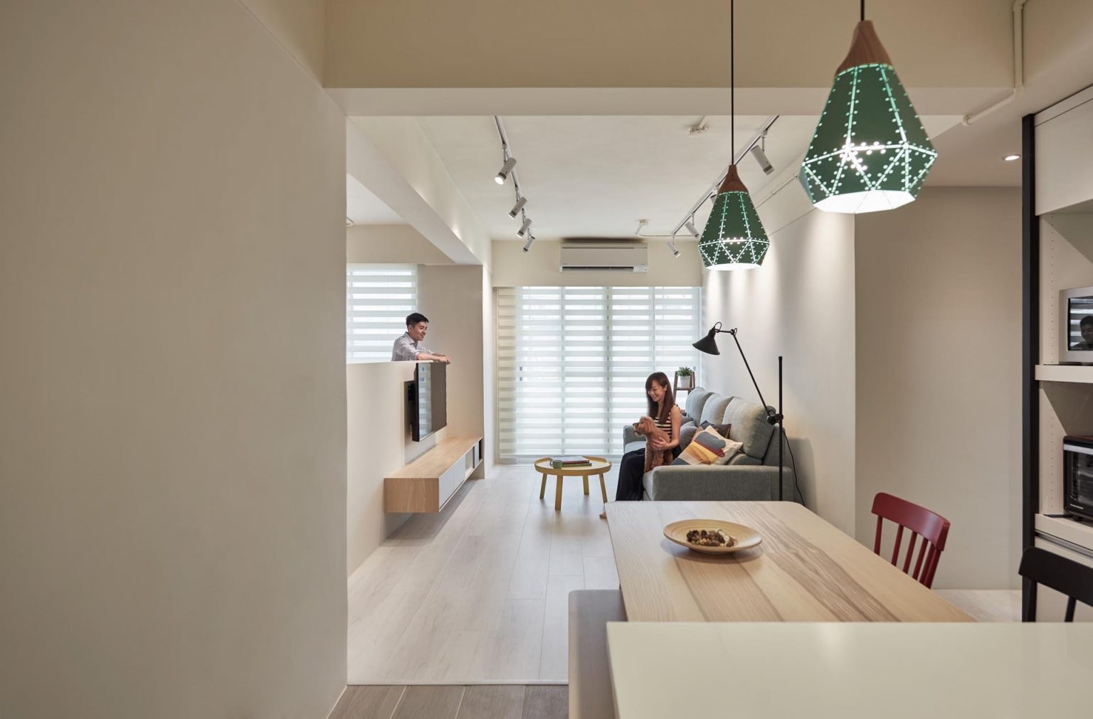 A hidden home office tucked behind a low partition wall, with a built-in desk, smart cable management, and an open connection to the living room.