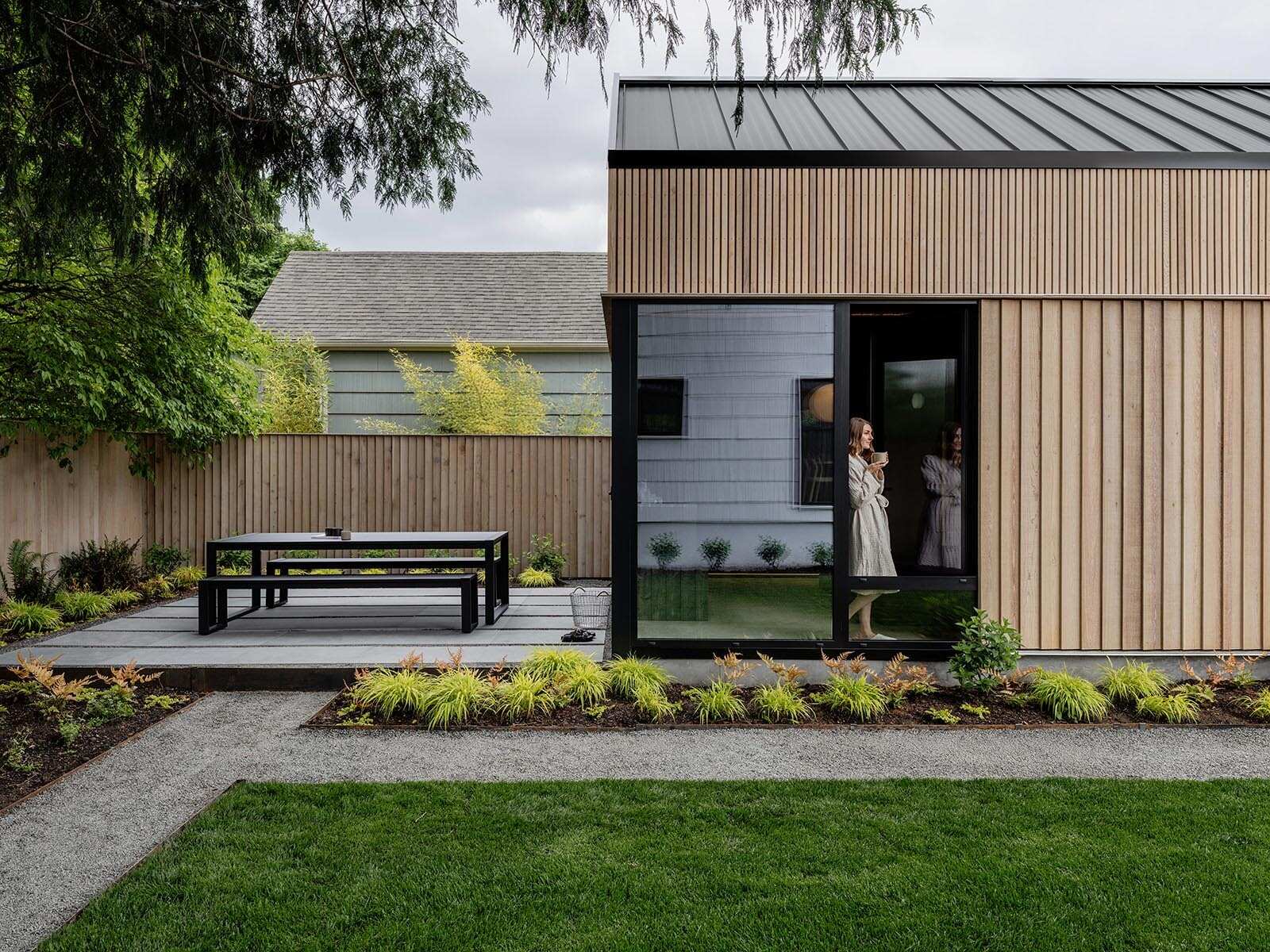 This cedar-clad bathhouse in Portland, Oregon transforms the footprint of a 100-year-old carriage house into a striking modern backyard spa. Designed by Ment Architecture with landscape design by Planterra Design, the project combines custom cedar siding, black steel details, lush layered planting, bluestone patios, and moody garden spaces inspired by Portland’s rainy winters.
