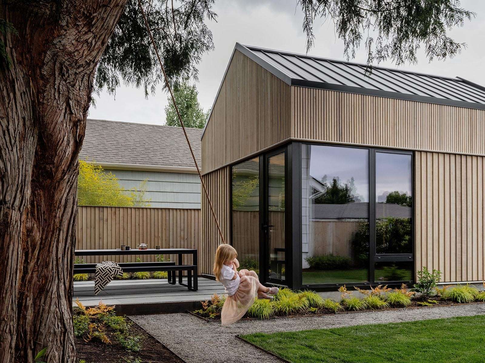 This cedar-clad bathhouse in Portland, Oregon transforms the footprint of a 100-year-old carriage house into a striking modern backyard spa. Designed by Ment Architecture with landscape design by Planterra Design, the project combines custom cedar siding, black steel details, lush layered planting, bluestone patios, and moody garden spaces inspired by Portland’s rainy winters.