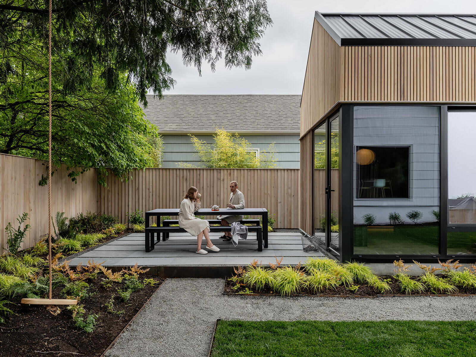 This cedar-clad bathhouse in Portland, Oregon transforms the footprint of a 100-year-old carriage house into a striking modern backyard spa. Designed by Ment Architecture with landscape design by Planterra Design, the project combines custom cedar siding, black steel details, lush layered planting, bluestone patios, and moody garden spaces inspired by Portland’s rainy winters.