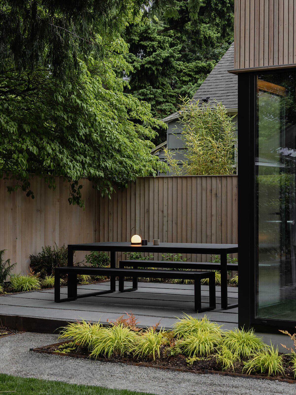 This cedar-clad bathhouse in Portland, Oregon transforms the footprint of a 100-year-old carriage house into a striking modern backyard spa. Designed by Ment Architecture with landscape design by Planterra Design, the project combines custom cedar siding, black steel details, lush layered planting, bluestone patios, and moody garden spaces inspired by Portland’s rainy winters.