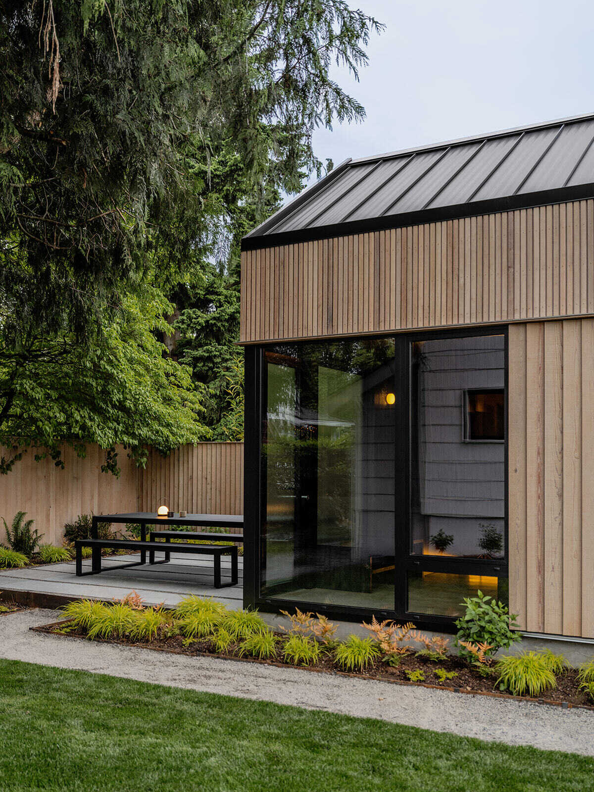 This cedar-clad bathhouse in Portland, Oregon transforms the footprint of a 100-year-old carriage house into a striking modern backyard spa. Designed by Ment Architecture with landscape design by Planterra Design, the project combines custom cedar siding, black steel details, lush layered planting, bluestone patios, and moody garden spaces inspired by Portland’s rainy winters.