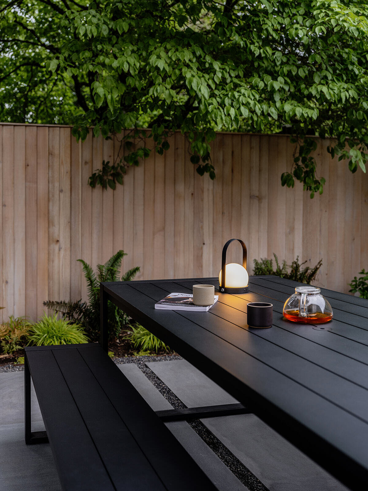 This cedar-clad bathhouse in Portland, Oregon transforms the footprint of a 100-year-old carriage house into a striking modern backyard spa. Designed by Ment Architecture with landscape design by Planterra Design, the project combines custom cedar siding, black steel details, lush layered planting, bluestone patios, and moody garden spaces inspired by Portland’s rainy winters.