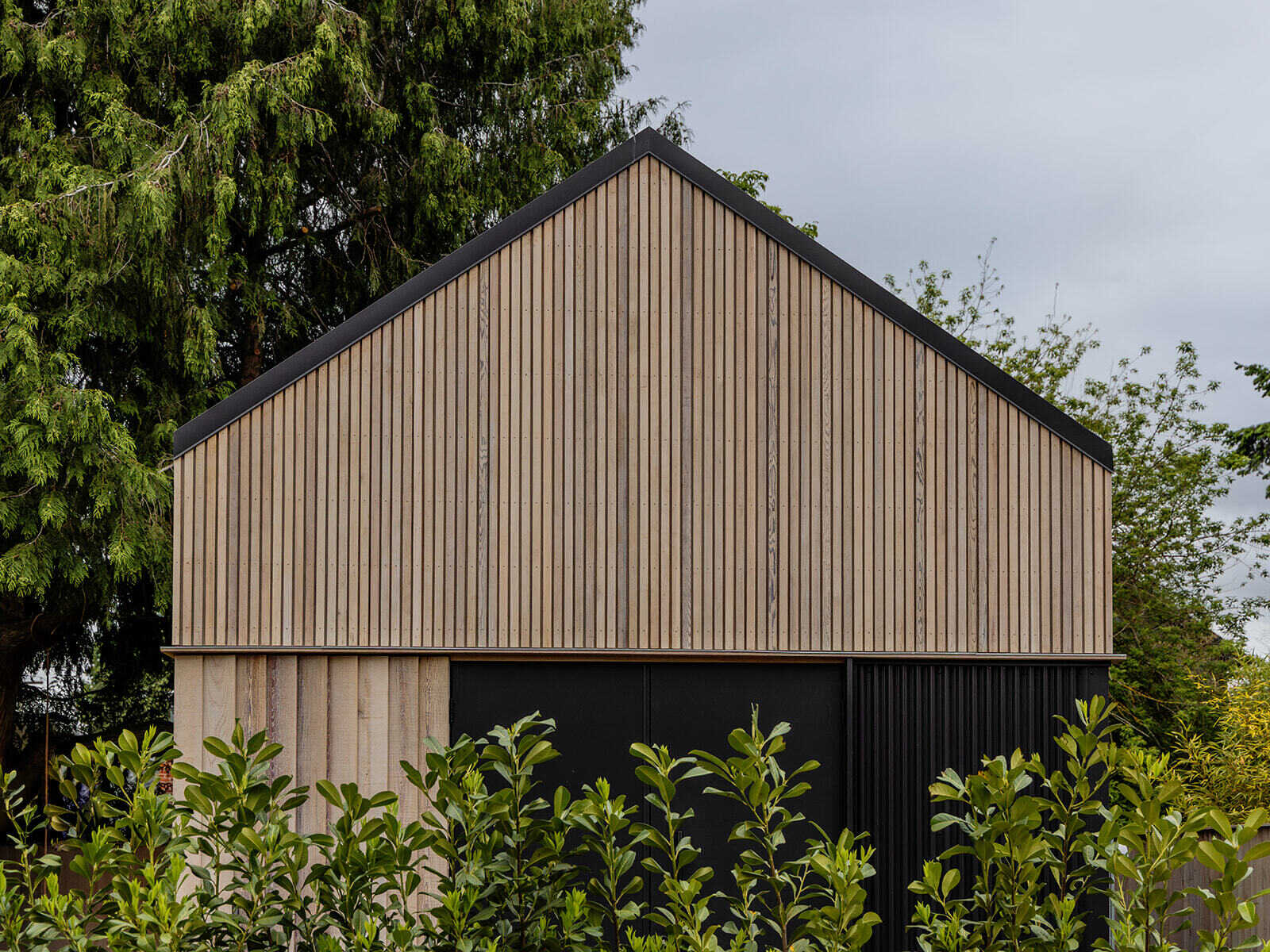 This cedar-clad bathhouse in Portland, Oregon transforms the footprint of a 100-year-old carriage house into a striking modern backyard spa. Designed by Ment Architecture with landscape design by Planterra Design, the project combines custom cedar siding, black steel details, lush layered planting, bluestone patios, and moody garden spaces inspired by Portland’s rainy winters.