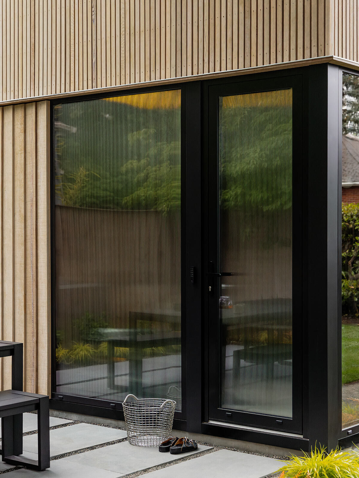 This cedar-clad bathhouse in Portland, Oregon transforms the footprint of a 100-year-old carriage house into a striking modern backyard spa. Designed by Ment Architecture with landscape design by Planterra Design, the project combines custom cedar siding, black steel details, lush layered planting, bluestone patios, and moody garden spaces inspired by Portland’s rainy winters.