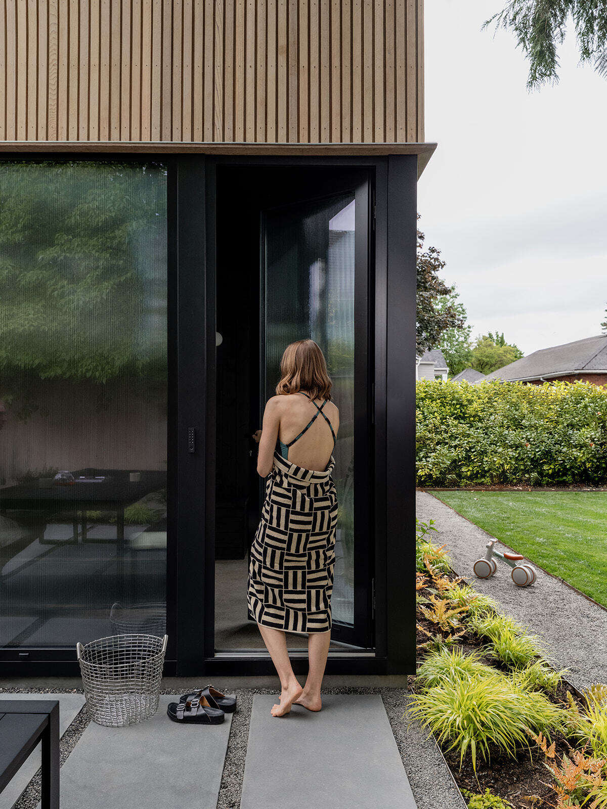 This cedar-clad bathhouse in Portland, Oregon transforms the footprint of a 100-year-old carriage house into a striking modern backyard spa. Designed by Ment Architecture with landscape design by Planterra Design, the project combines custom cedar siding, black steel details, lush layered planting, bluestone patios, and moody garden spaces inspired by Portland’s rainy winters.