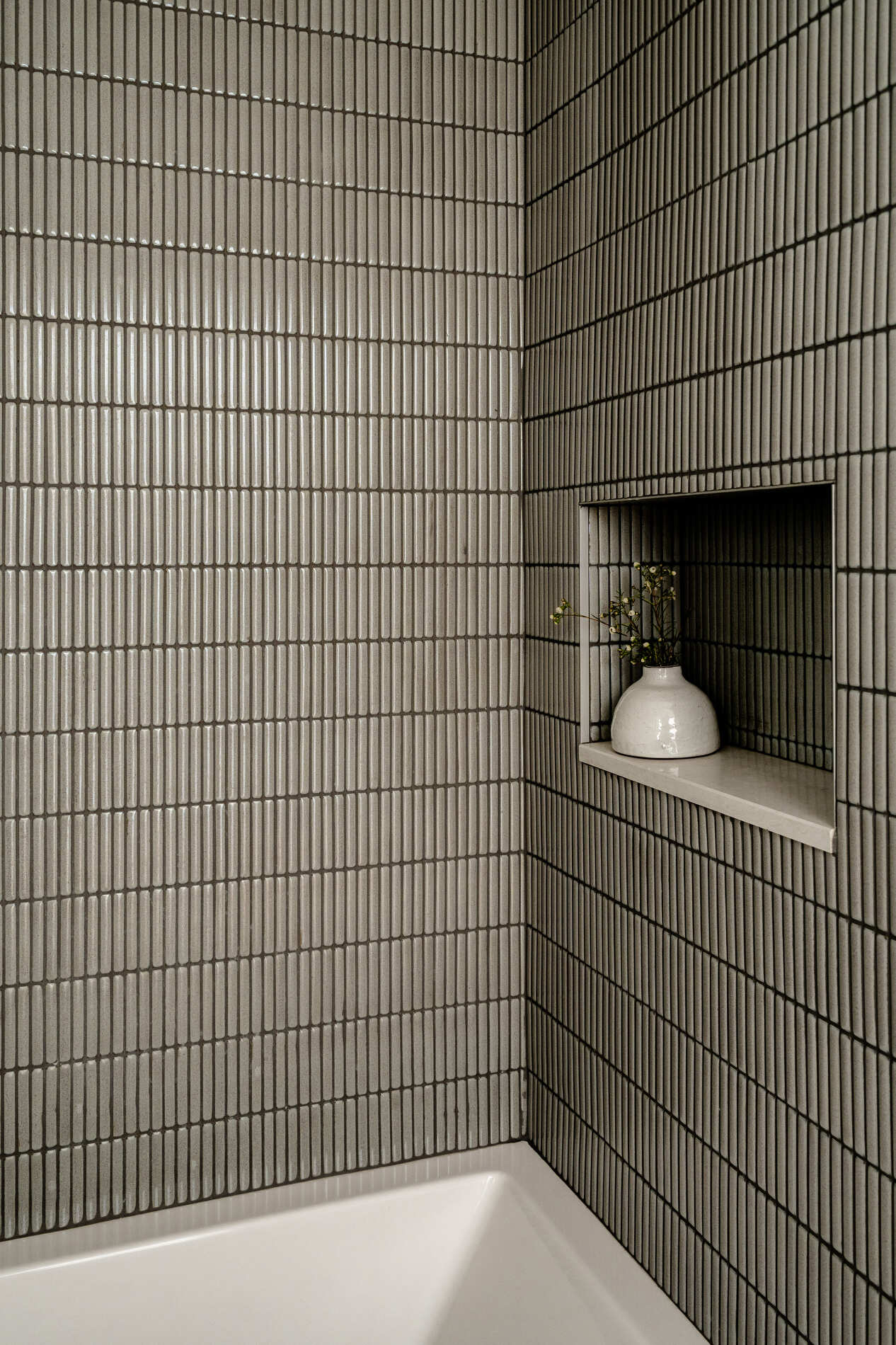 A modern bathroom with thin vertical 'kit-kat' style tiles and a shelving niche.