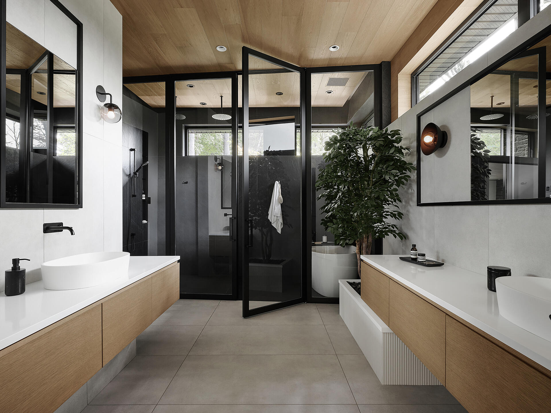 The bathroom features a pair of vanities, integrated lighting, and a wet room with dark tile surfaces and a glass wall that separates it from the rest of the room. The use of natural materials helps the spaces feel consistent with the rest of the residence while still maintaining a quieter atmosphere.