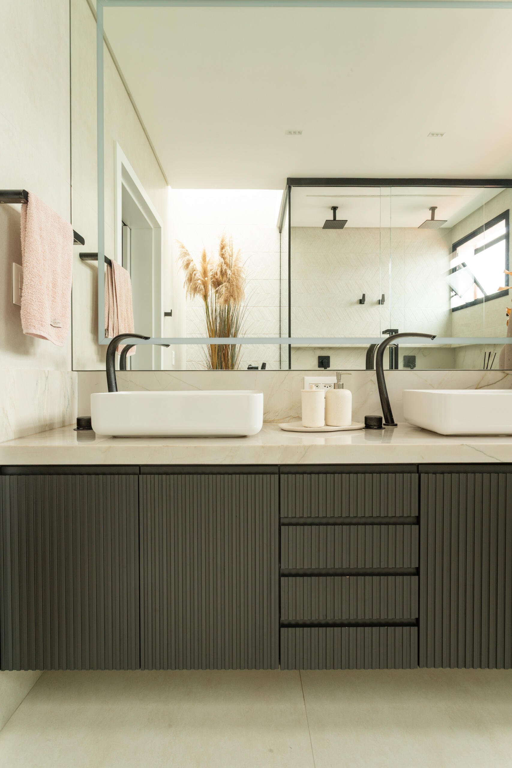 This contemporary primary bathroom features soft neutral stone, black framed glass, floating cabinetry, and minimalist detailing inside Casa R|L in Brazil.