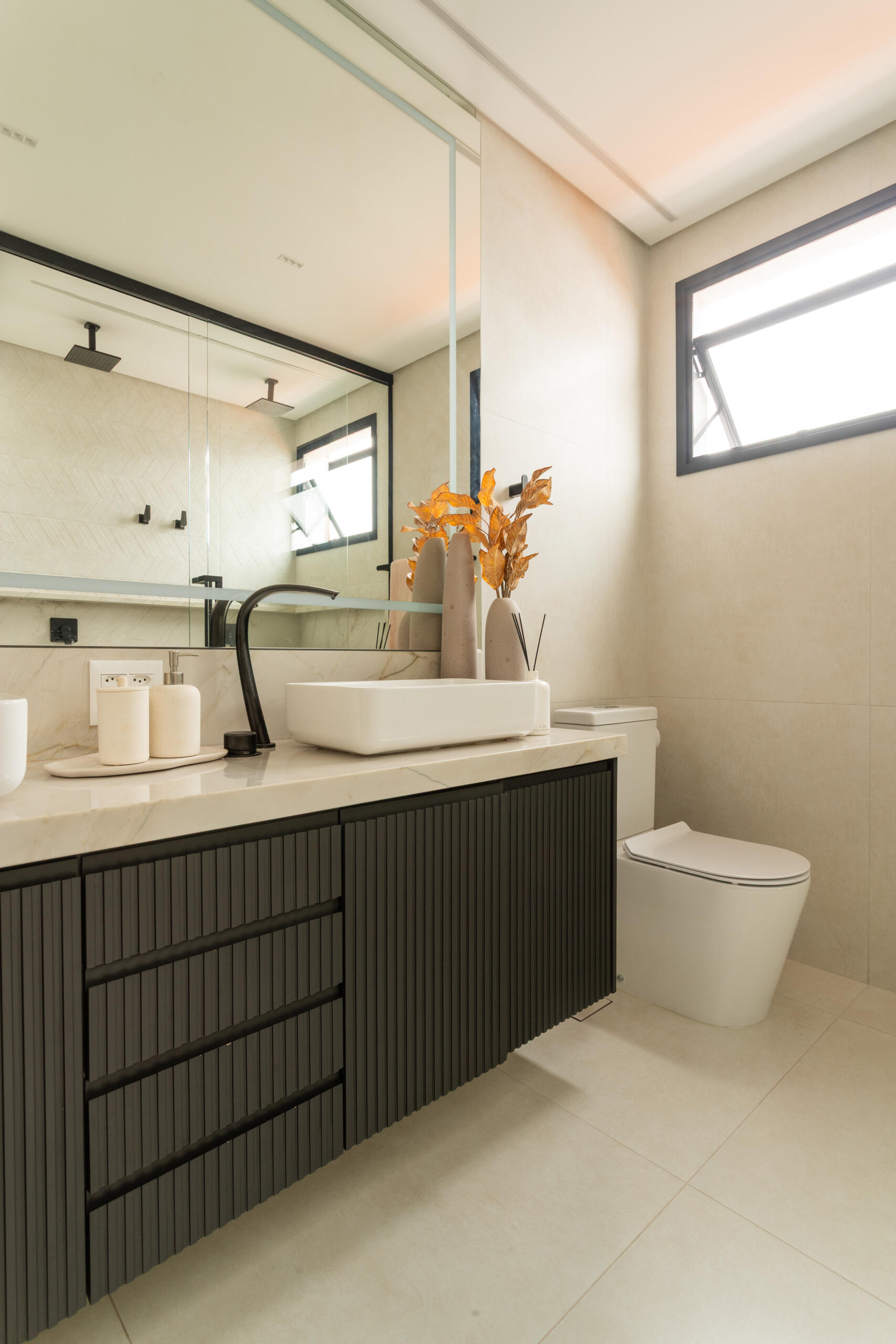 This contemporary primary bathroom features soft neutral stone, black framed glass, floating cabinetry, and minimalist detailing inside Casa R|L in Brazil.