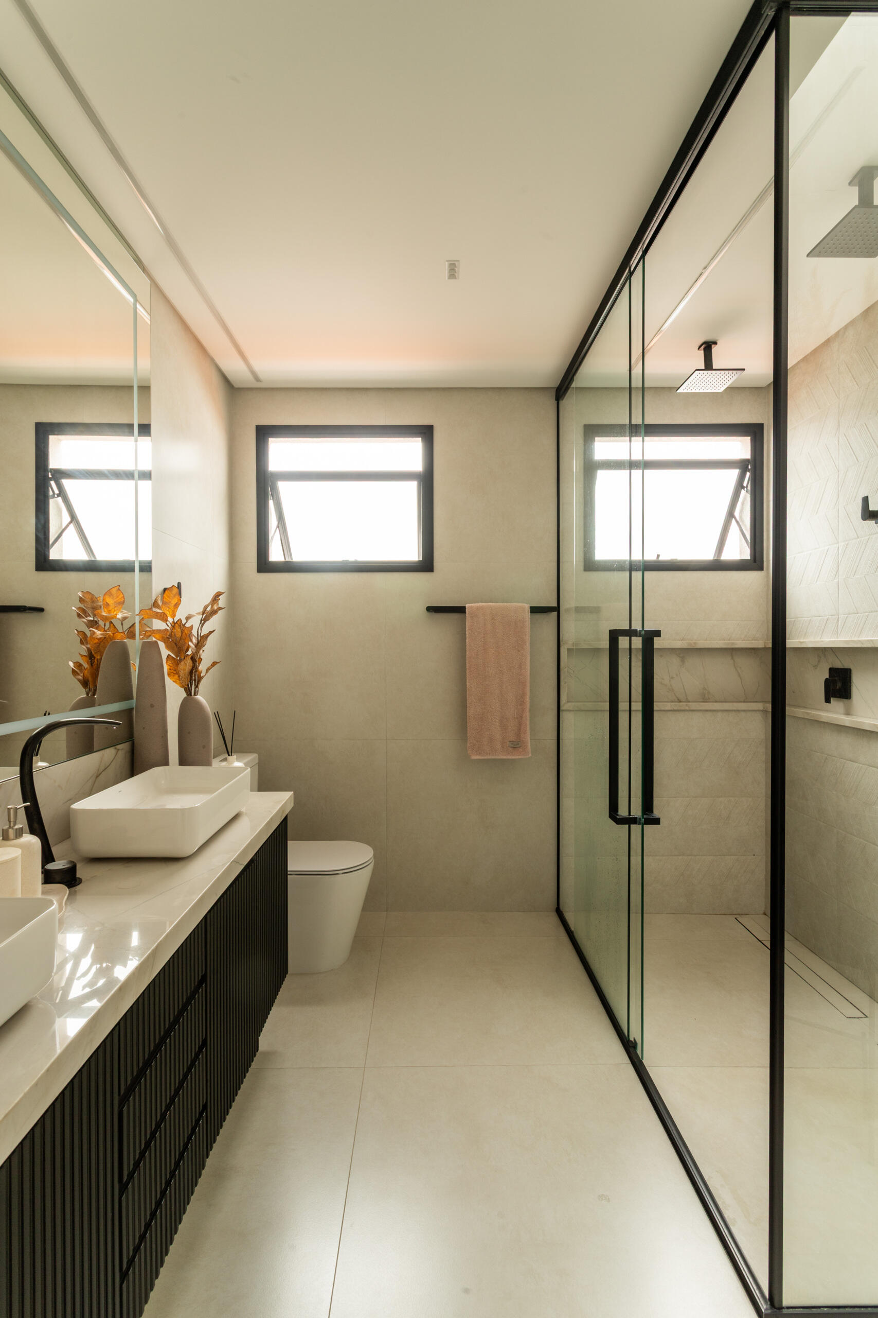 This contemporary primary bathroom features soft neutral stone, black framed glass, floating cabinetry, and minimalist detailing inside Casa R|L in Brazil.