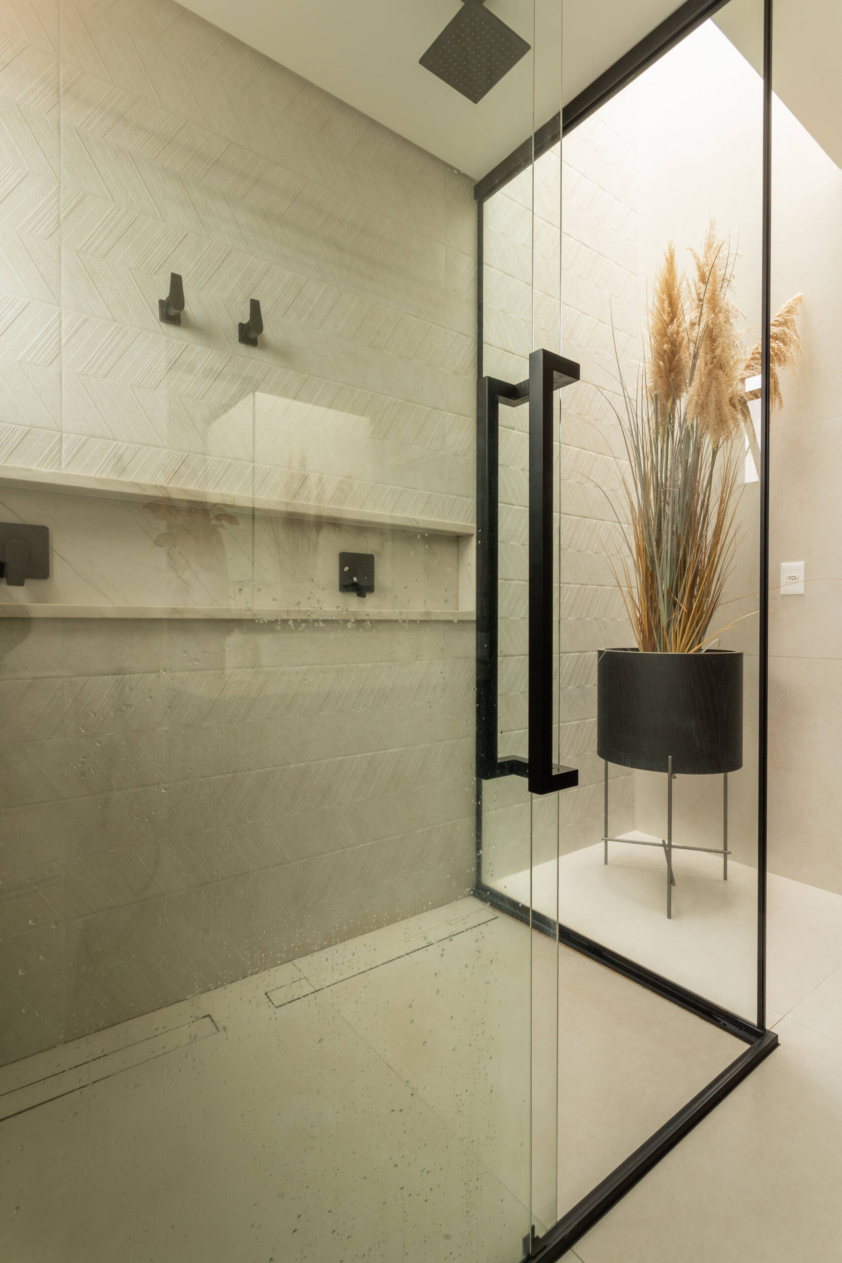 This contemporary primary bathroom features soft neutral stone, black framed glass, floating cabinetry, and minimalist detailing inside Casa R|L in Brazil.