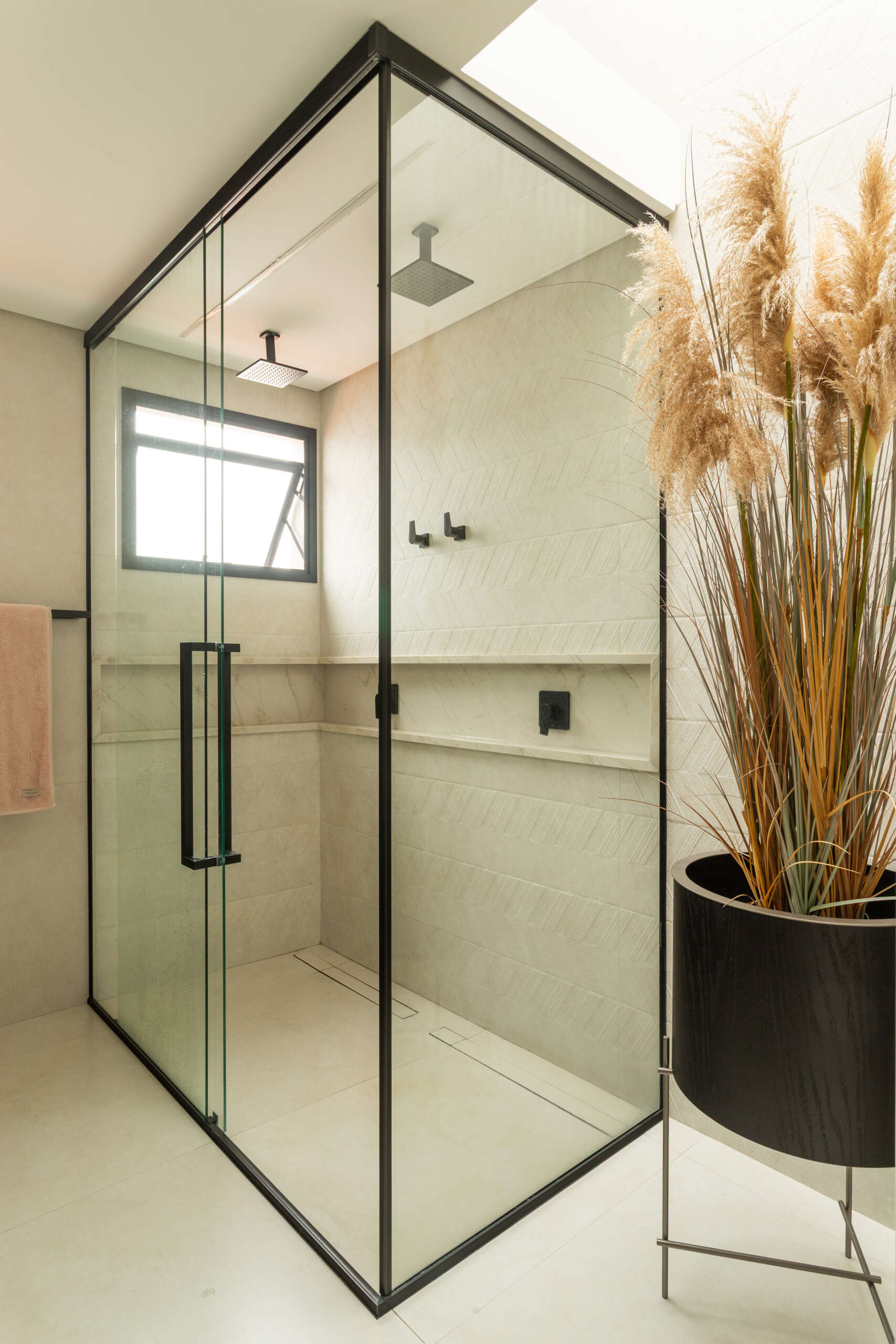 This contemporary primary bathroom features soft neutral stone, black framed glass, floating cabinetry, and minimalist detailing inside Casa R|L in Brazil.