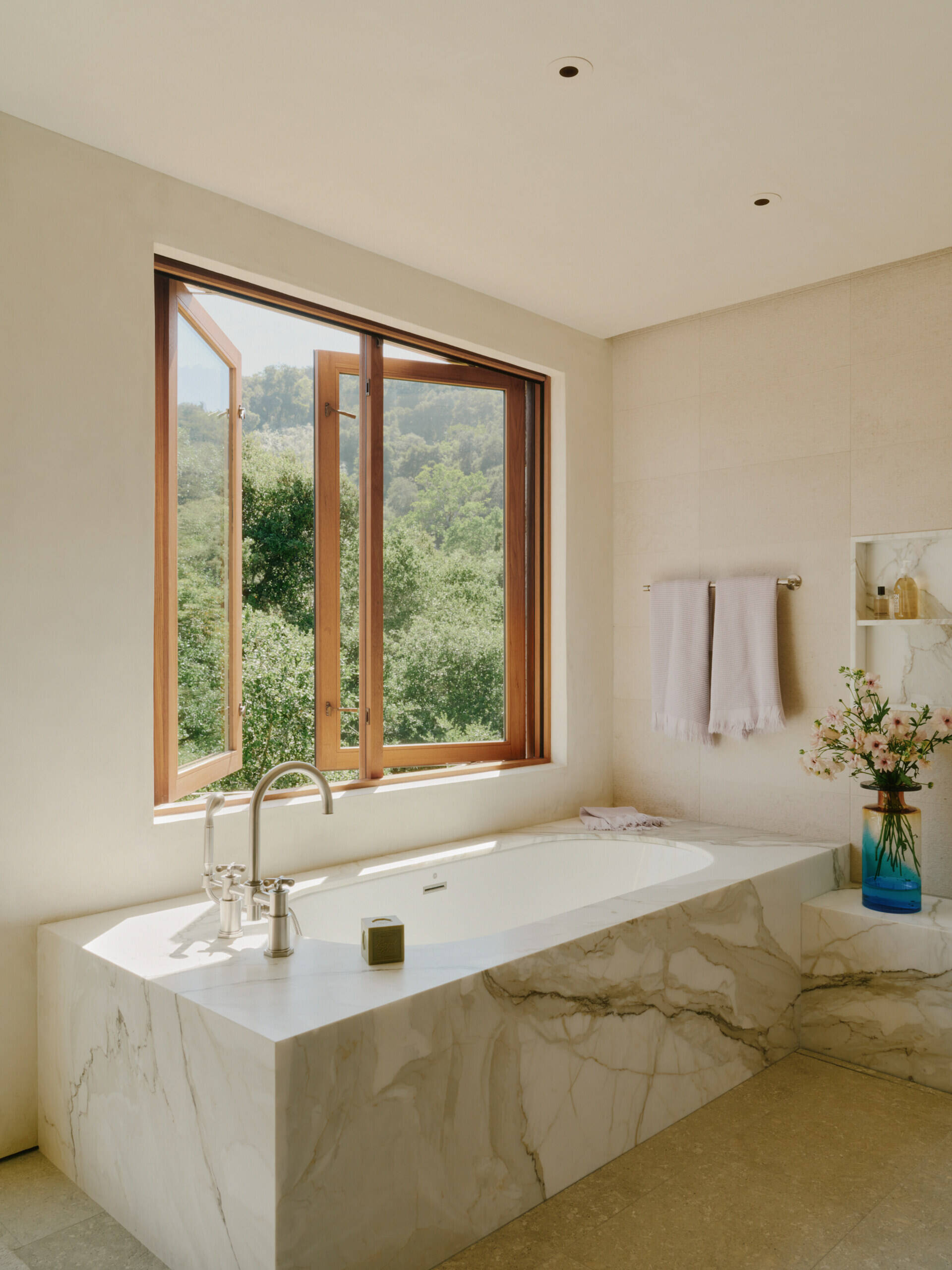 Stone textures, warm wood, and filtered natural light shape the peaceful bathroom interiors inside this California villa.