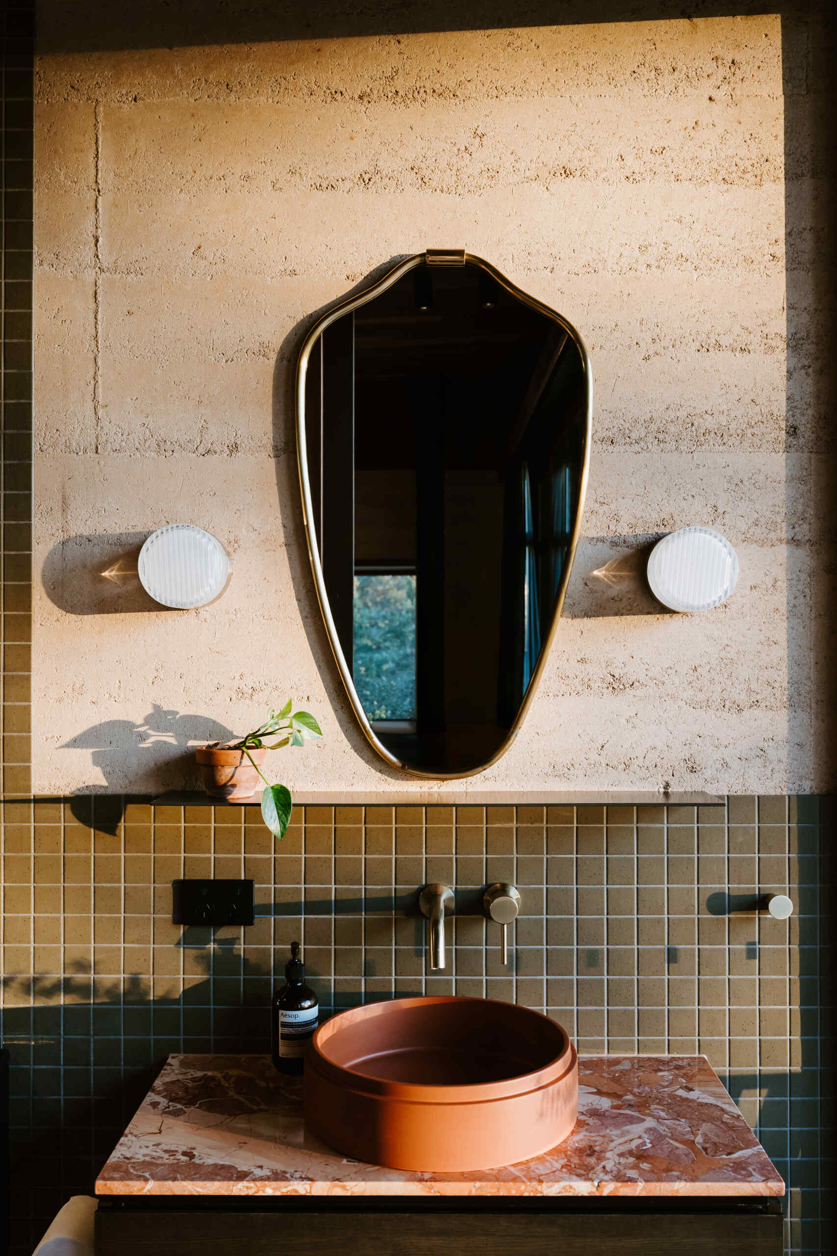 A modern off-grid cabin with rammed earth walls and sage green square tiles in the bathroom.