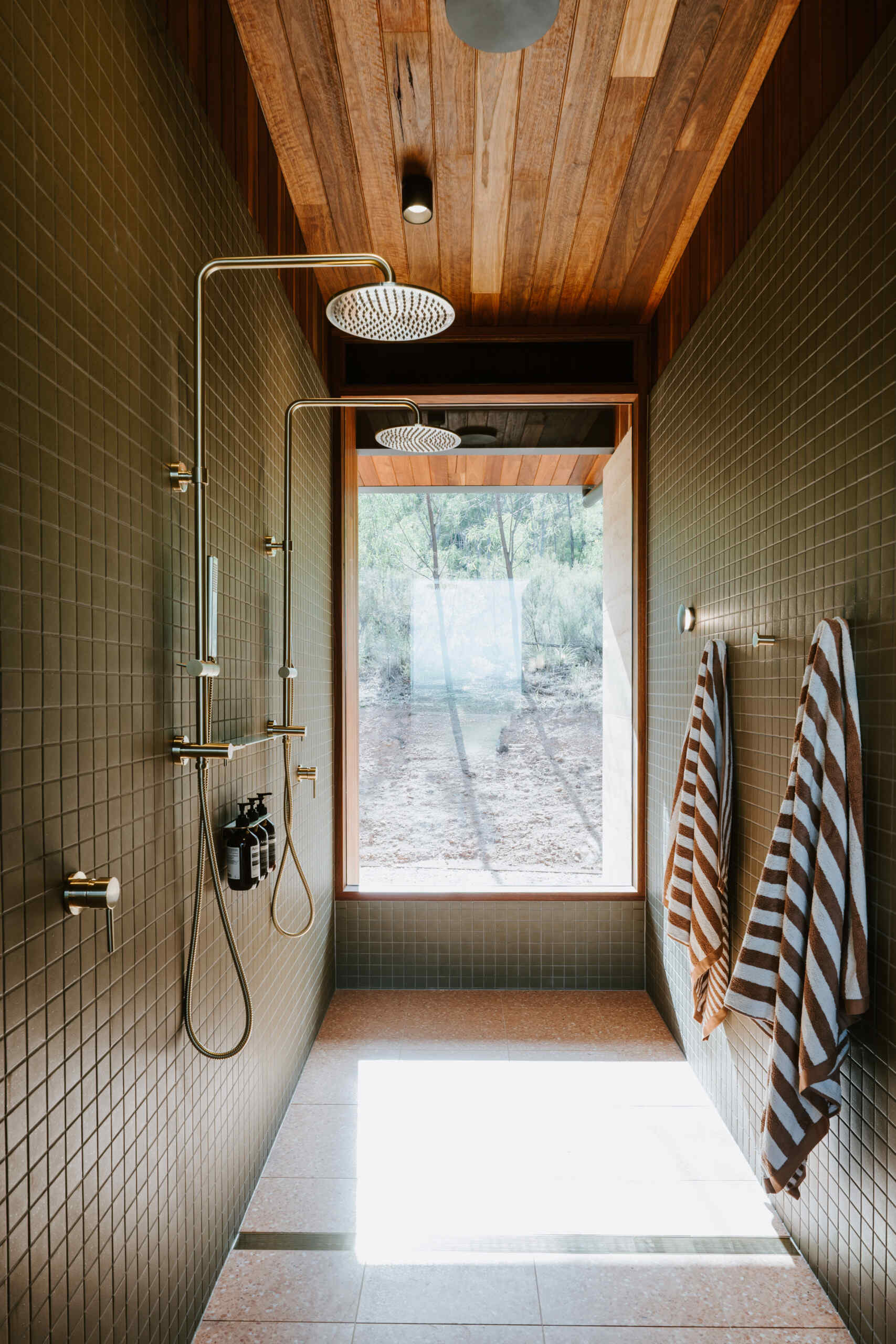 A modern off-grid cabin with rammed earth walls and sage green square tiles in the bathroom.