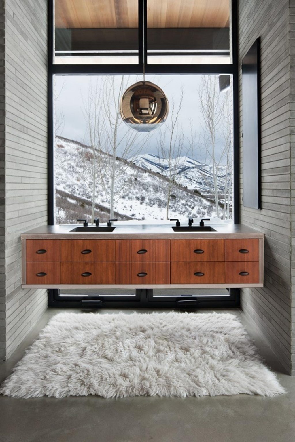 A floating wood-and-concrete vanity sits directly in front of a large window, turning everyday routines into an experience shaped by the landscape. Natural materials and expansive views make this bathroom a standout feature of Quarry House.